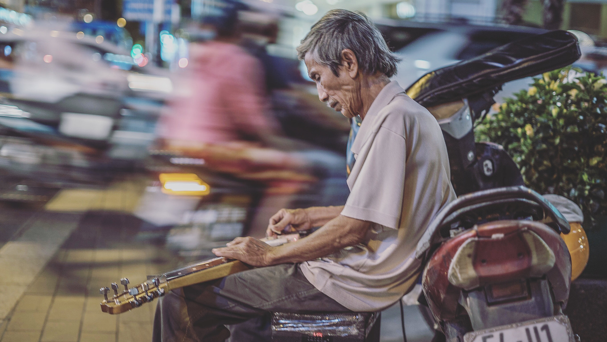 Sony a7S II + Sony FE 50mm F1.8 sample photo. A busker plays slide guitar as traffic goes by. ho chi minh city, vietnam photography