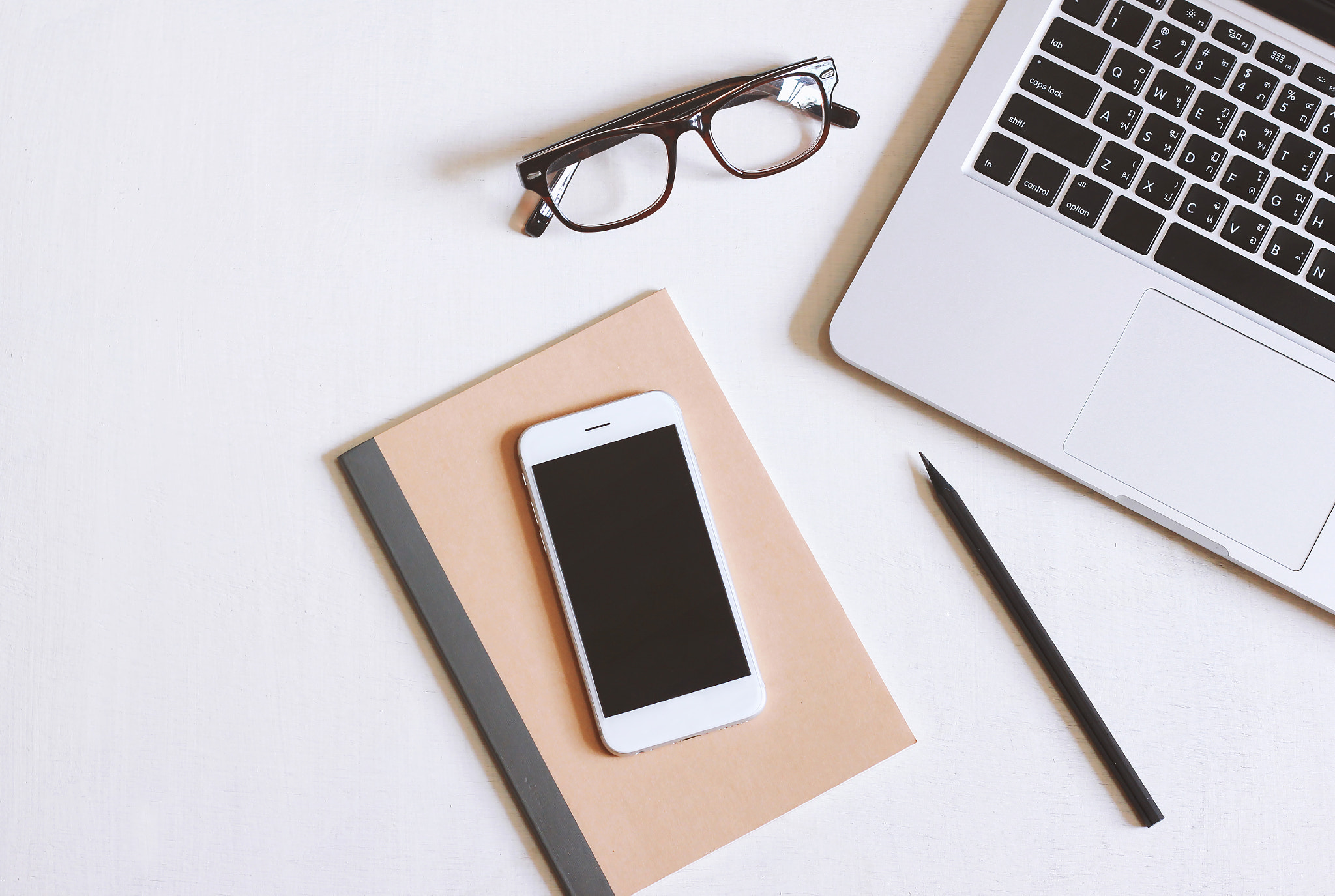 Flat lay photo of office desk with laptop, smartphone, eyeglasse