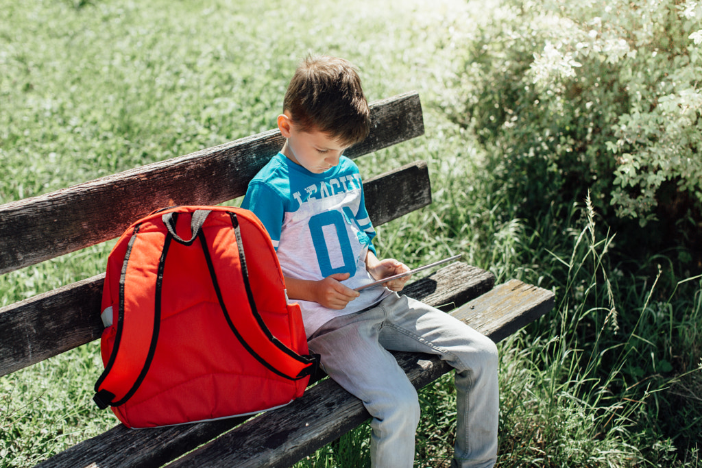 Schoolboy on bench taking break playing on tablet by Newman Studio on 500px.com