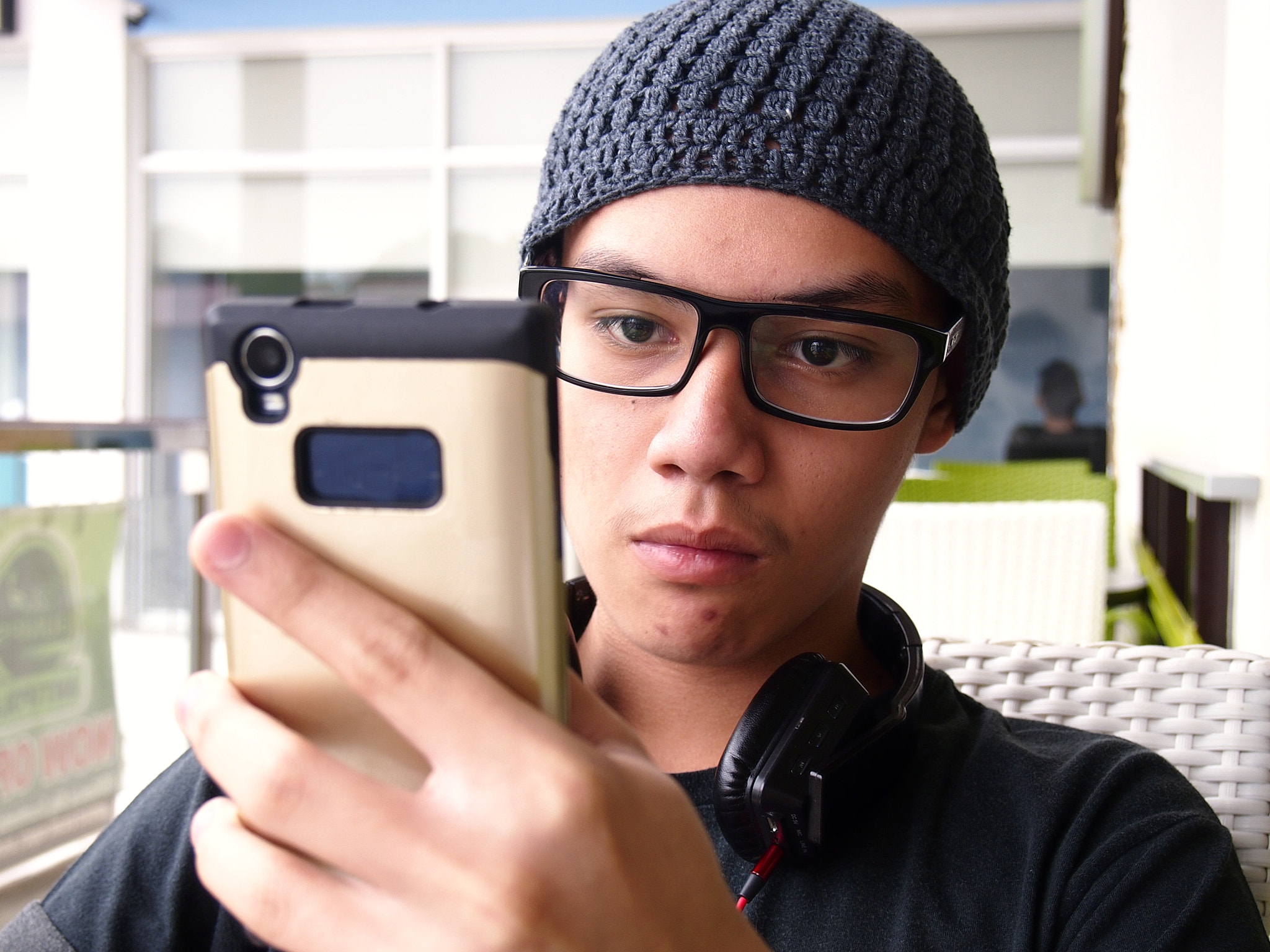 Teenager wearing a bonnet and eyeglasses using a smartphone
