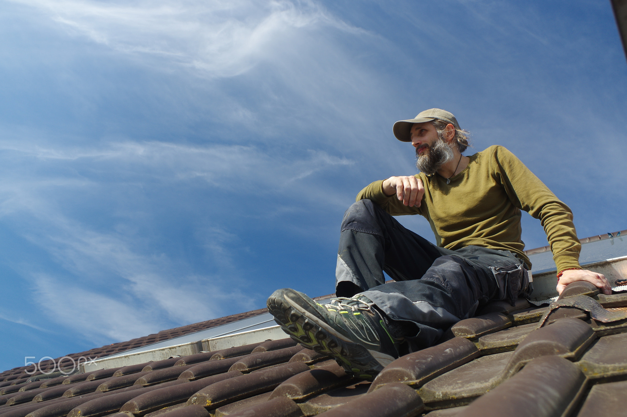 bearded roofer resting on top of a roof sunny day