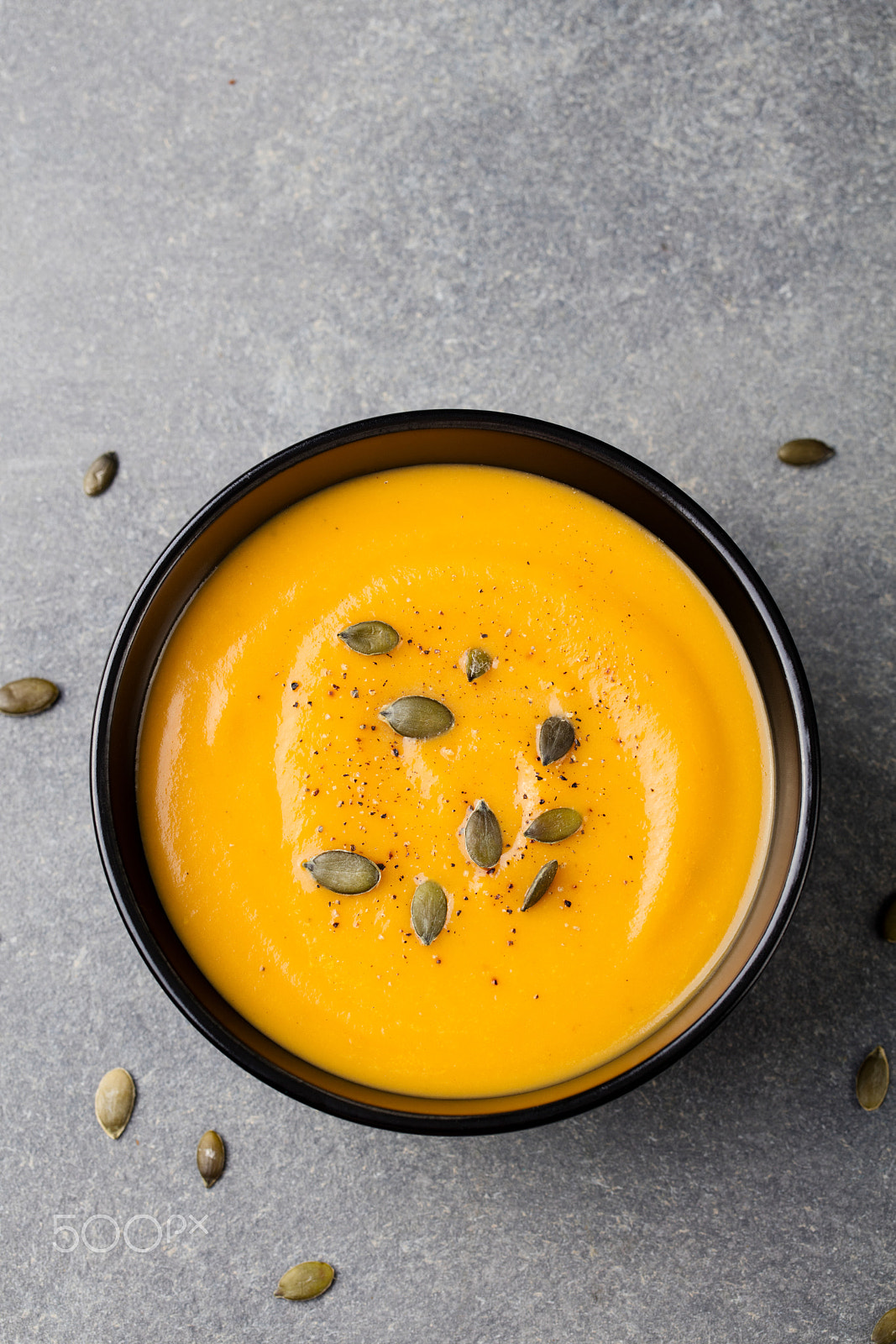 Canon EOS 5DS + Canon EF 100mm F2.8L Macro IS USM sample photo. Pumpkin cream soup with pumpkin seeds in a black bowl. grey stone background. top view copy space photography