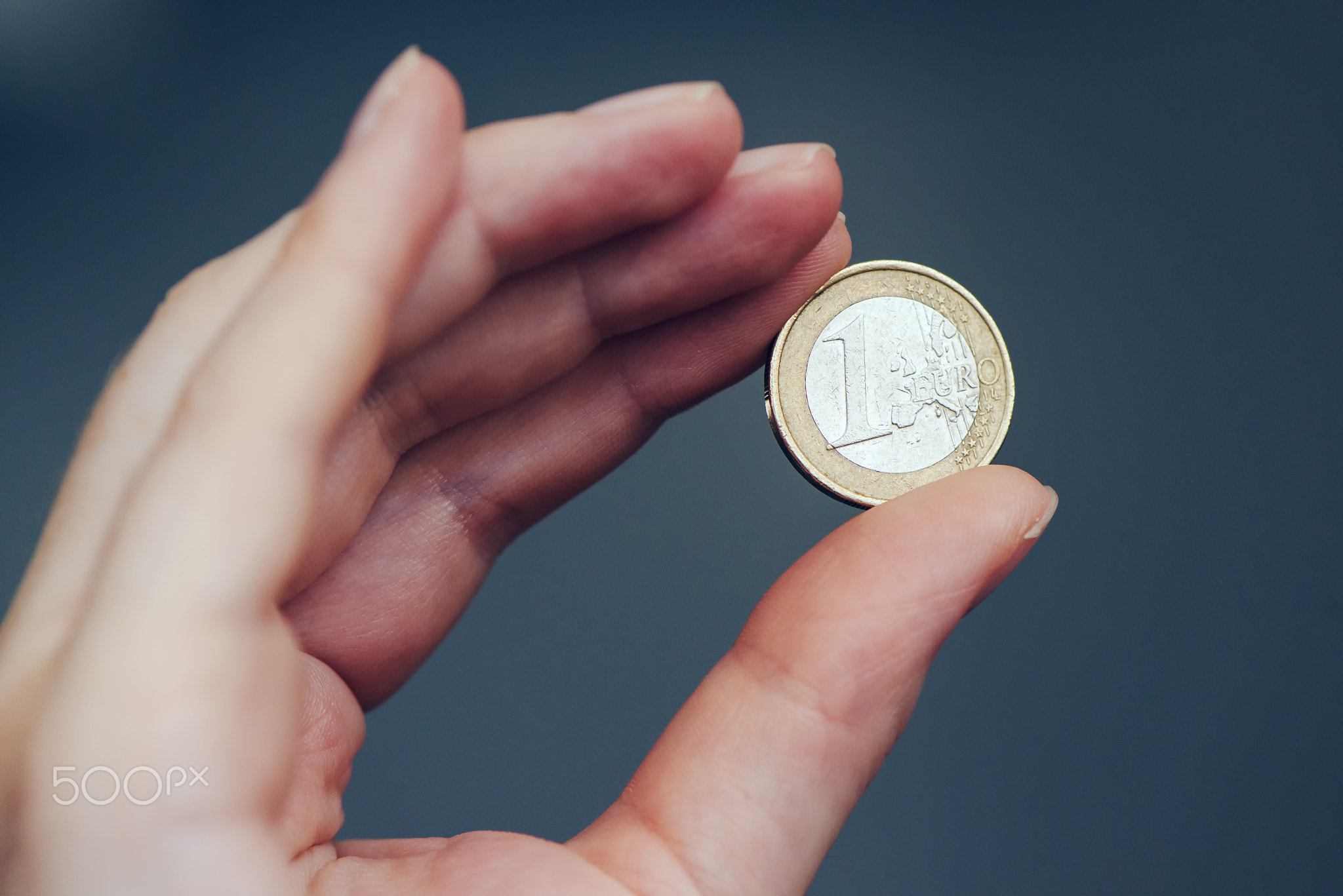 Business woman holding one euro coin between fingers