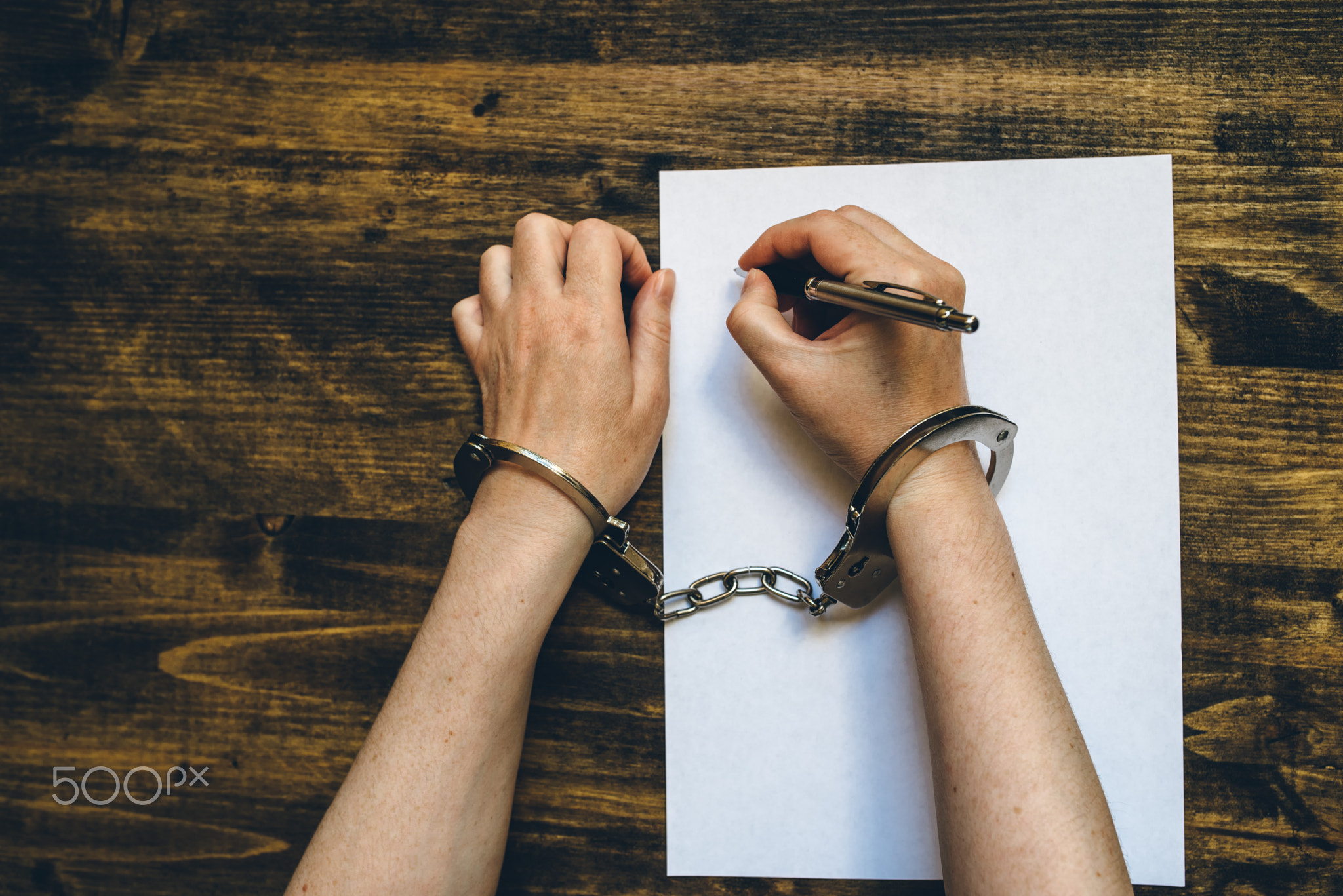 Female hands cuffed signing confession, top view