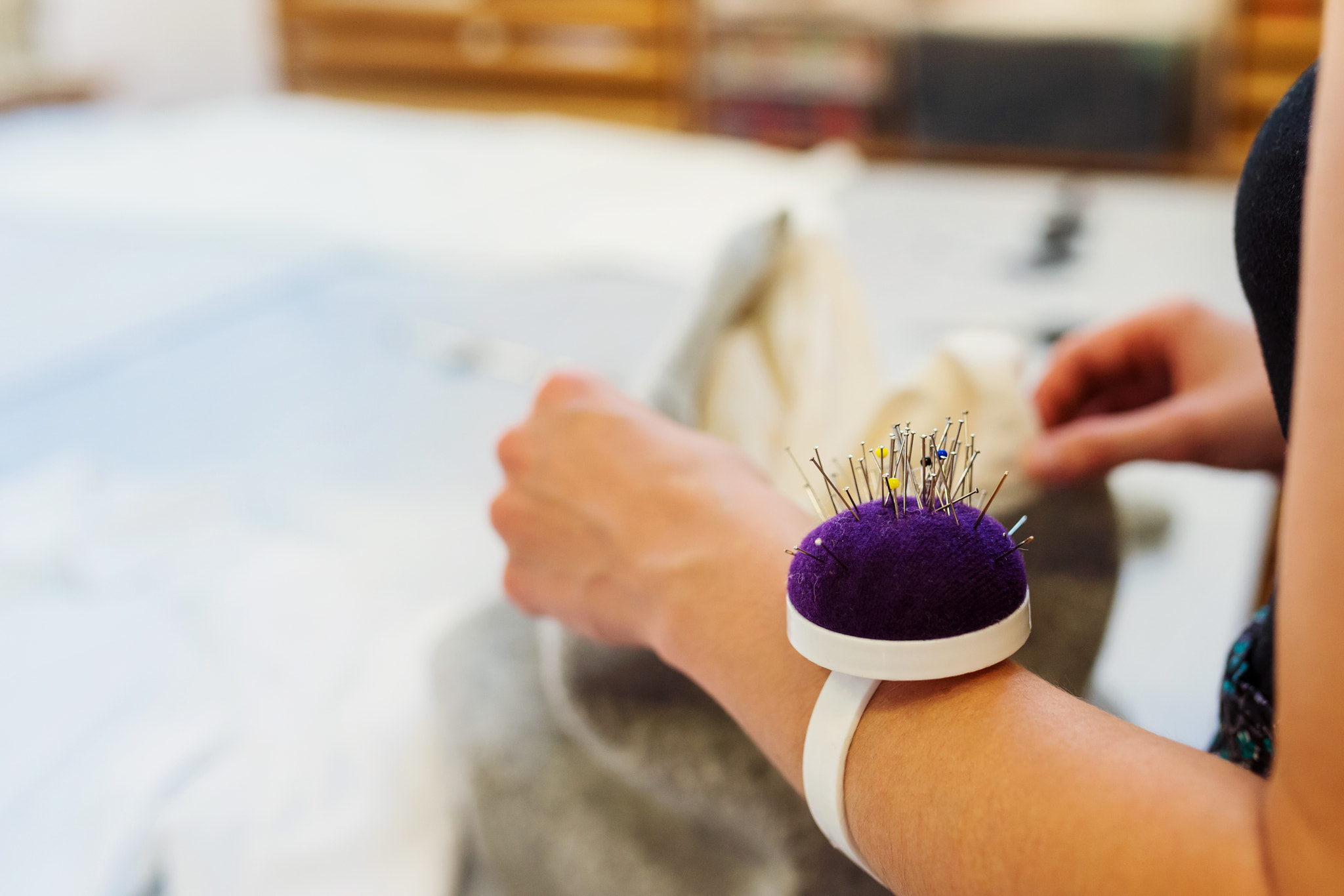 Hands of unrecognizable tailor woman with pin cushion working
