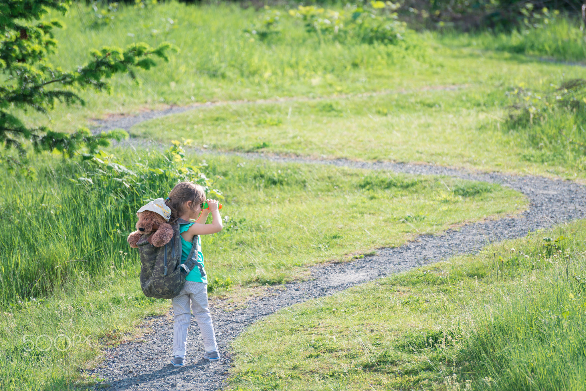 Girl with teddy bear in backpack looking at the trail ahead