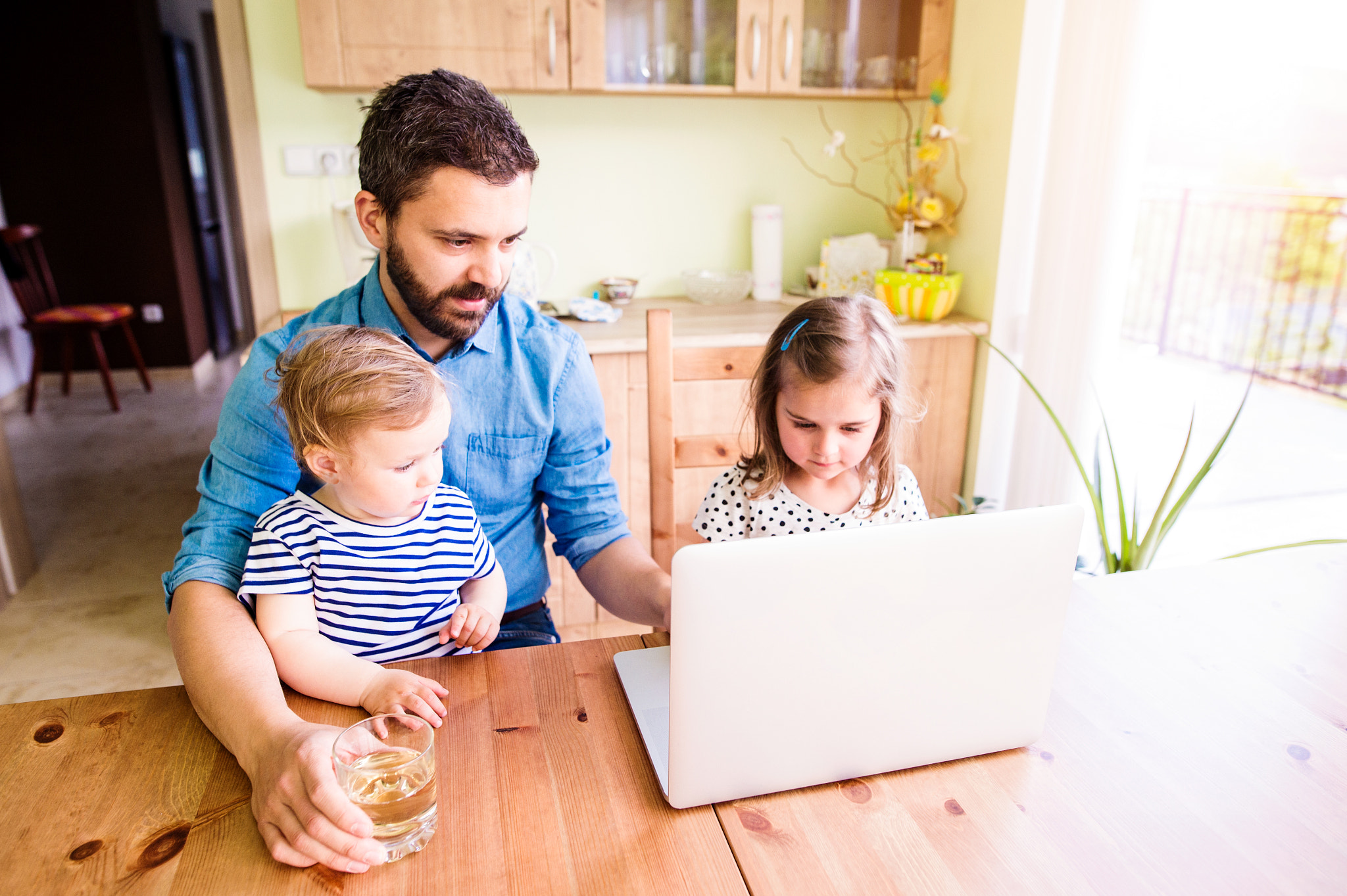 Father and daughters, playing on laptop, sitting in kitchen