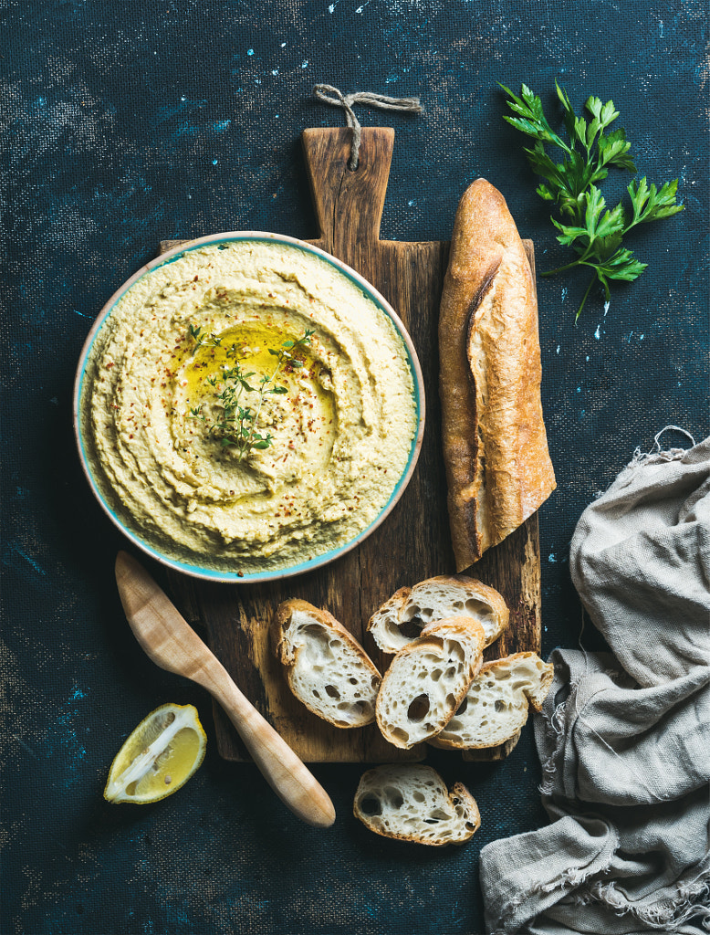 Homemade hummus in bowl with lemon, herbs and baguette by Anna Ivanova on 500px.com