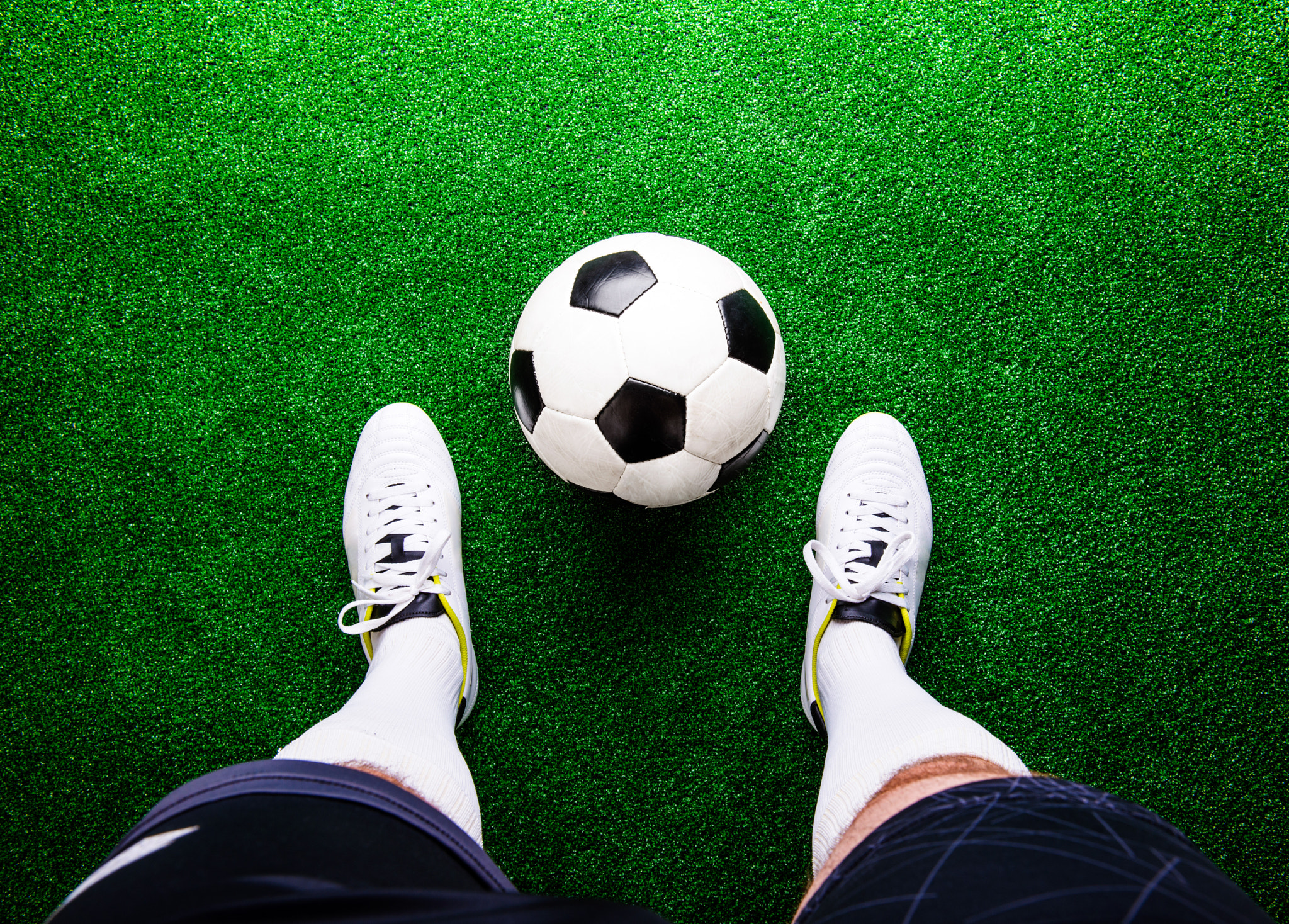 Unrecognizable football player against green grass, studio shot