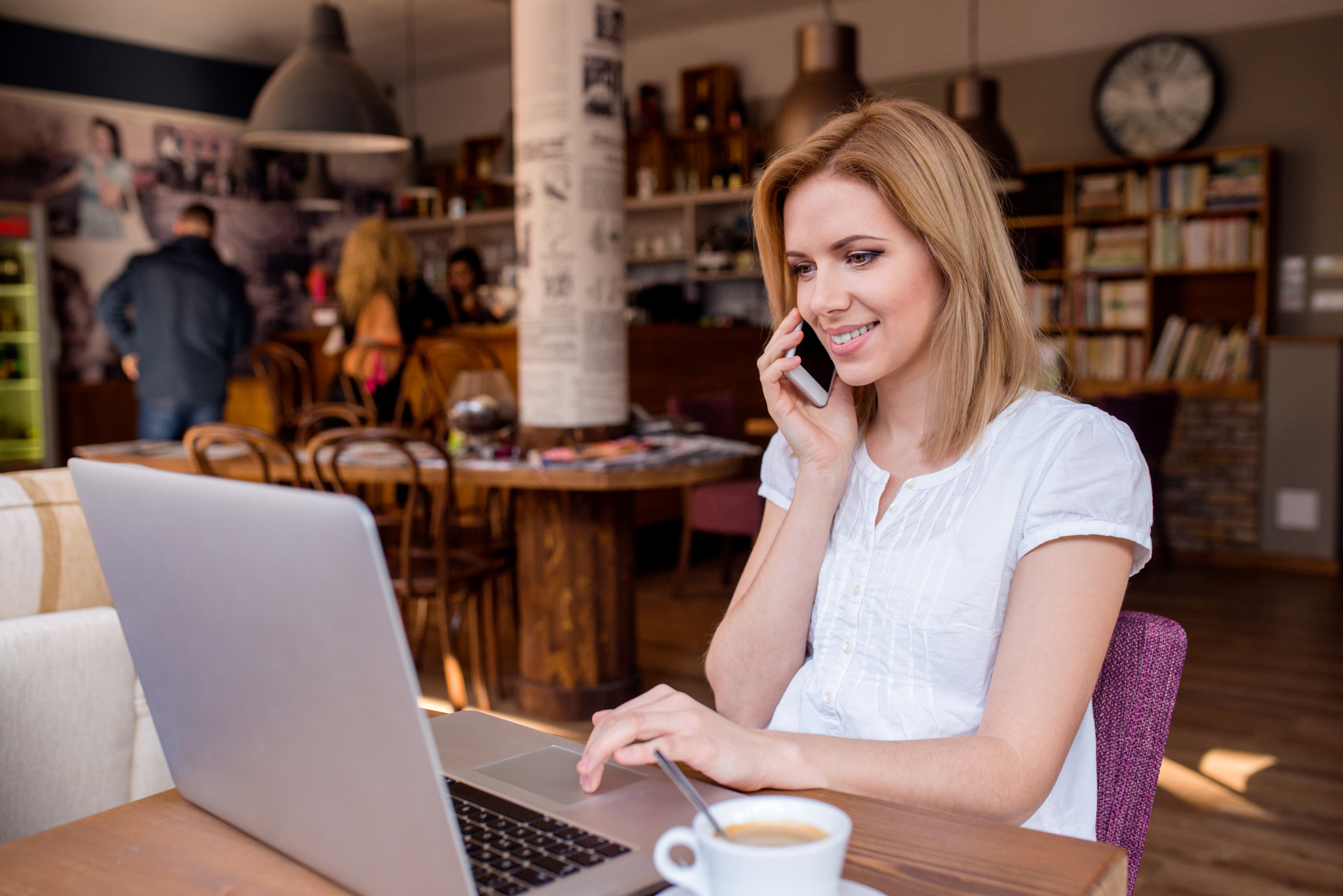 Woman in cafe, talking on phone, working on notebook