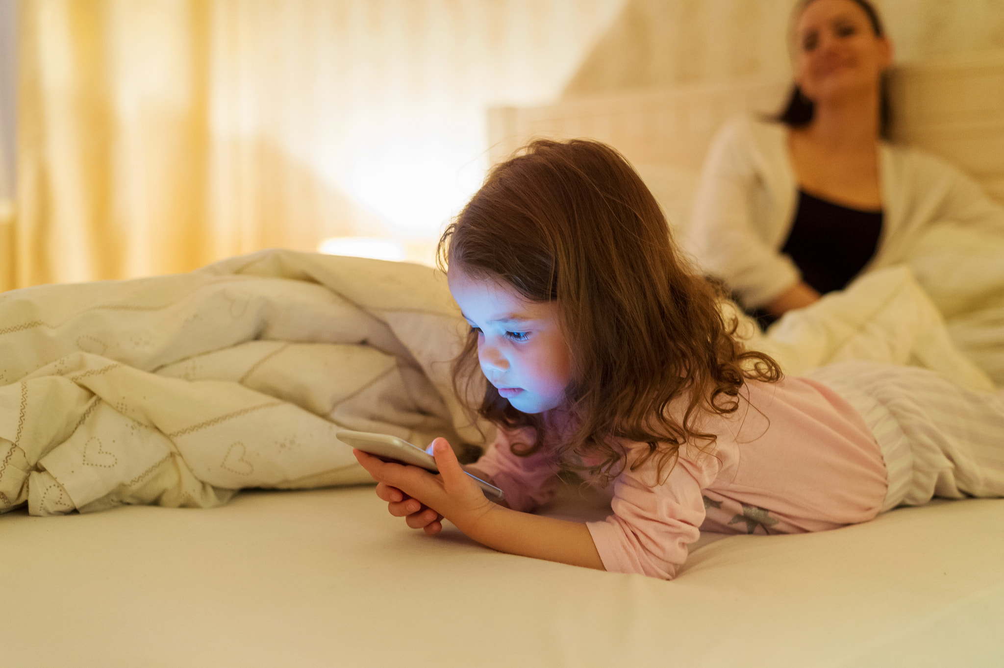 Nikon D4S sample photo. Little girl with smartphone lying in a bed, bedtime photography