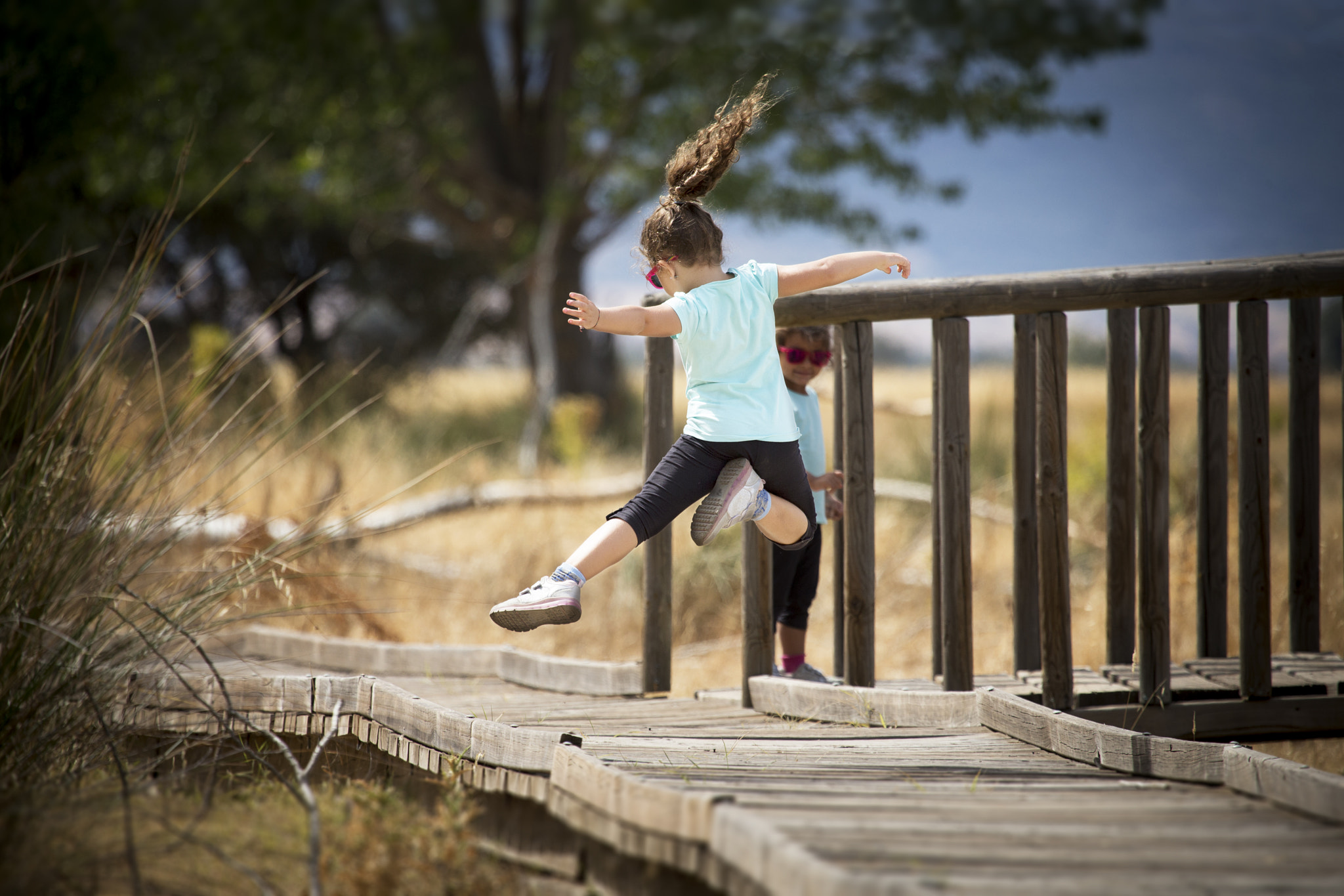 Canon EF 100-400mm F4.5-5.6L IS USM sample photo. Jovial kid jumping in mid-air on wooden path photography