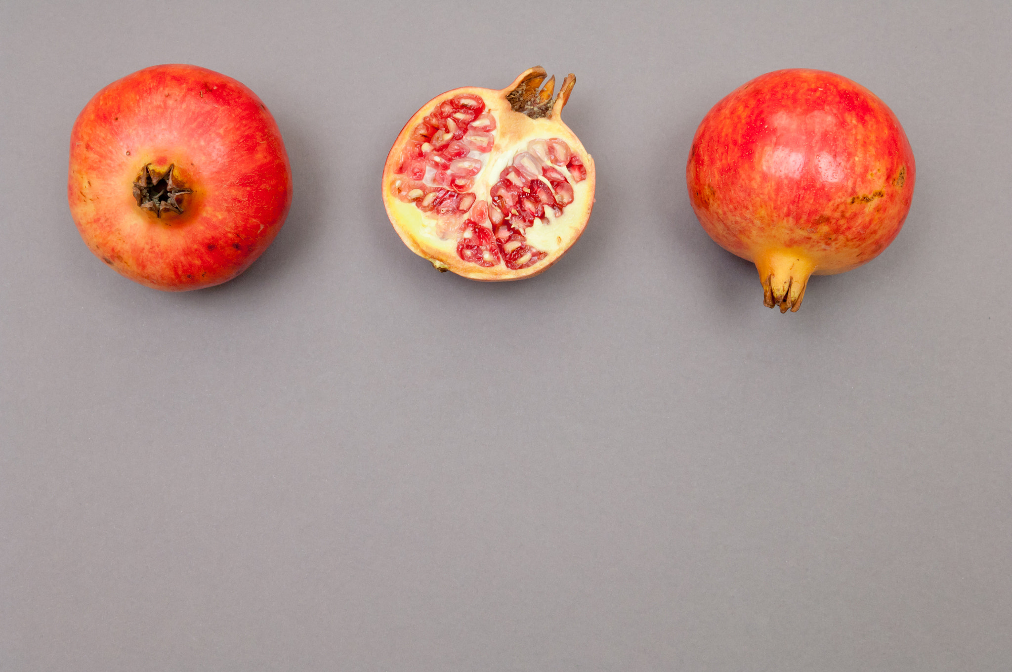 Nikon D2X sample photo. Whole and cut pomegranates in row on grey background photography