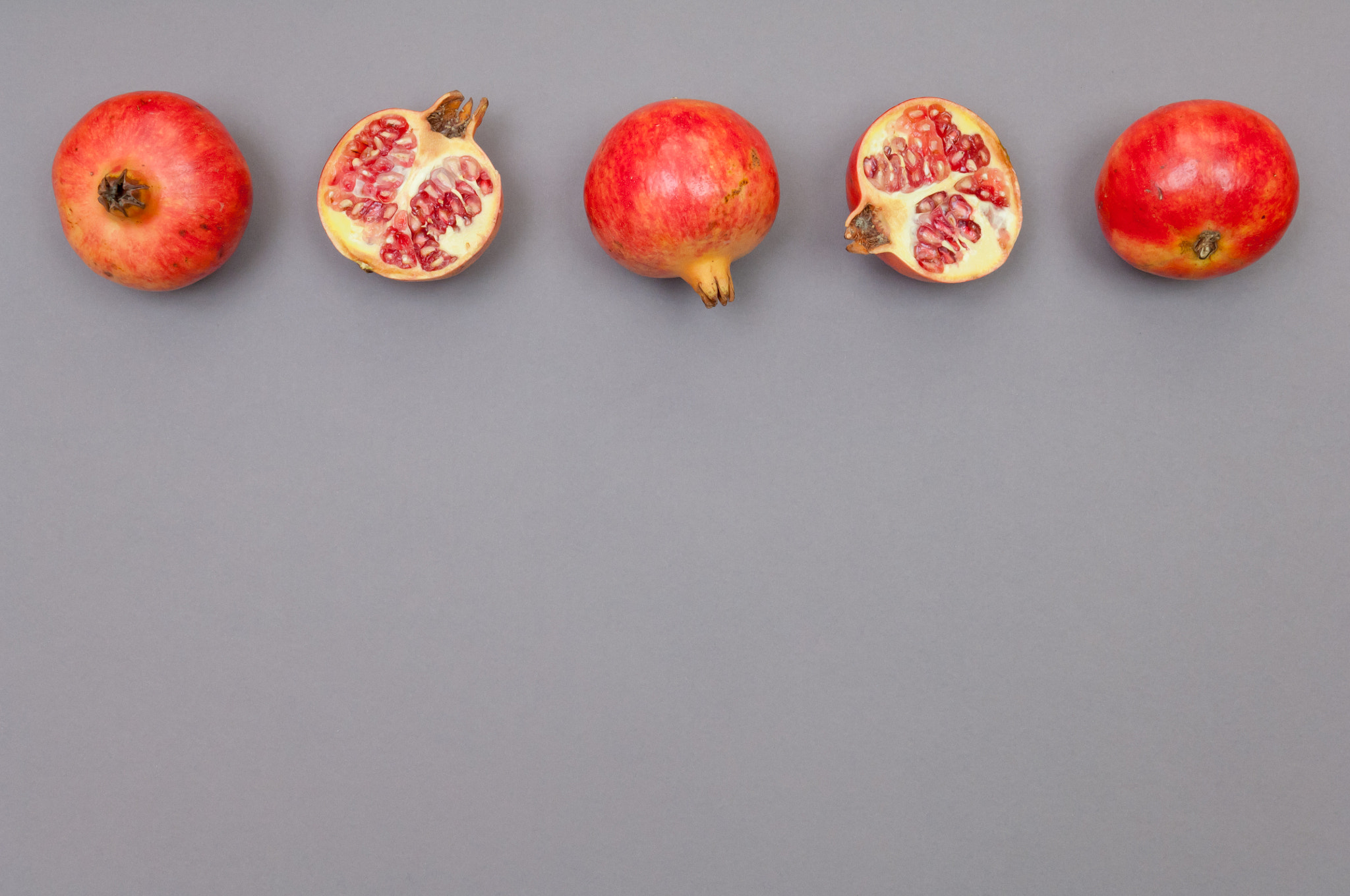 Nikon D2X sample photo. Whole and cut pomegranates in row on  grey background photography