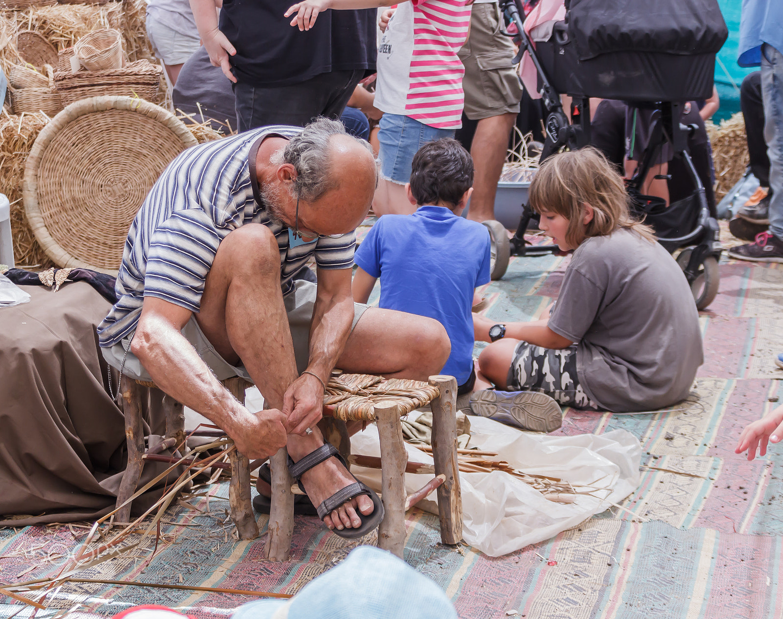 Canon EOS 600D (Rebel EOS T3i / EOS Kiss X5) + Canon EF 75-300mm F4.0-5.6 IS USM sample photo. Elderly man weaves chair at the fair photography