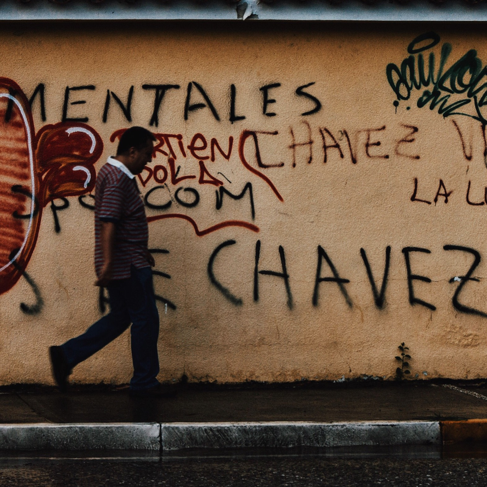Sony Alpha DSLR-A290 sample photo. Man walks in the city, face a wall full of reference written the former president hugo chavez. photography