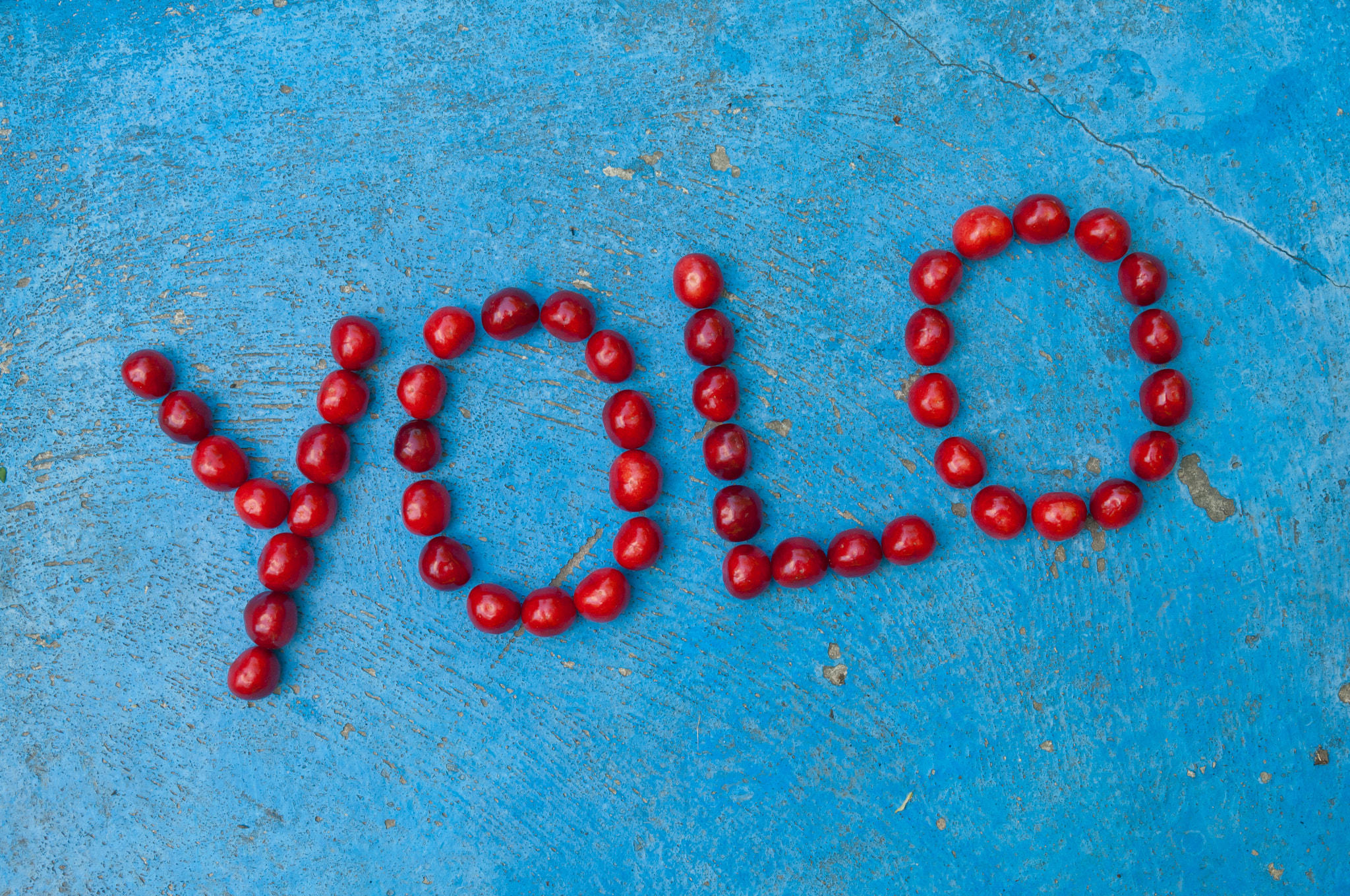 Nikon D2X + Nikon AF-S DX Nikkor 17-55mm F2.8G ED-IF sample photo. Cherries arranged to form the word yolo on blue background photography