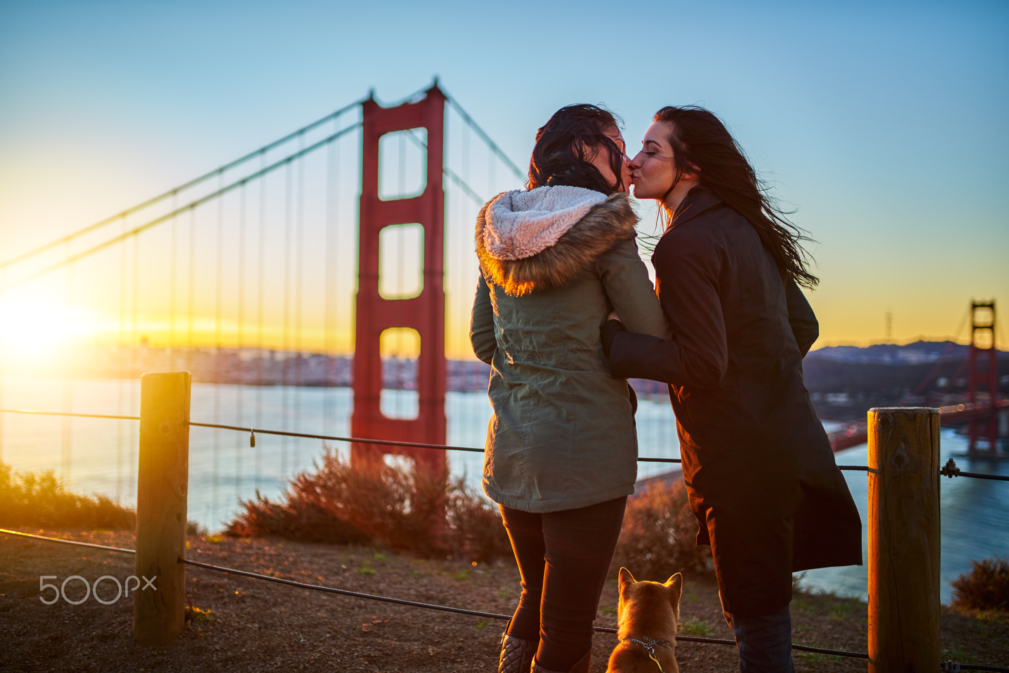 romantic lesbian couple kissing at golden gate bridge with pet dog