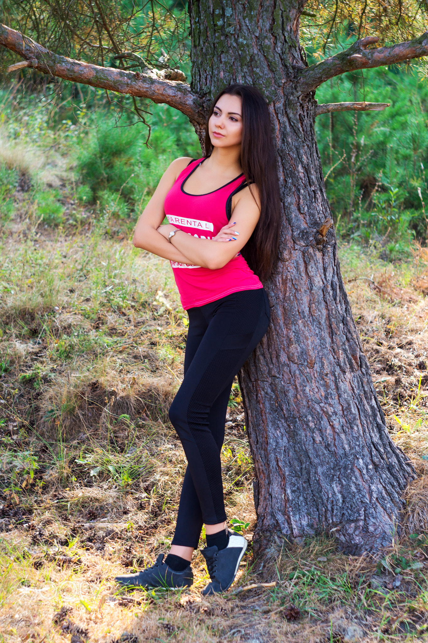 Young beautiful brunette model posing in the sports image of the park against the backdrop trees