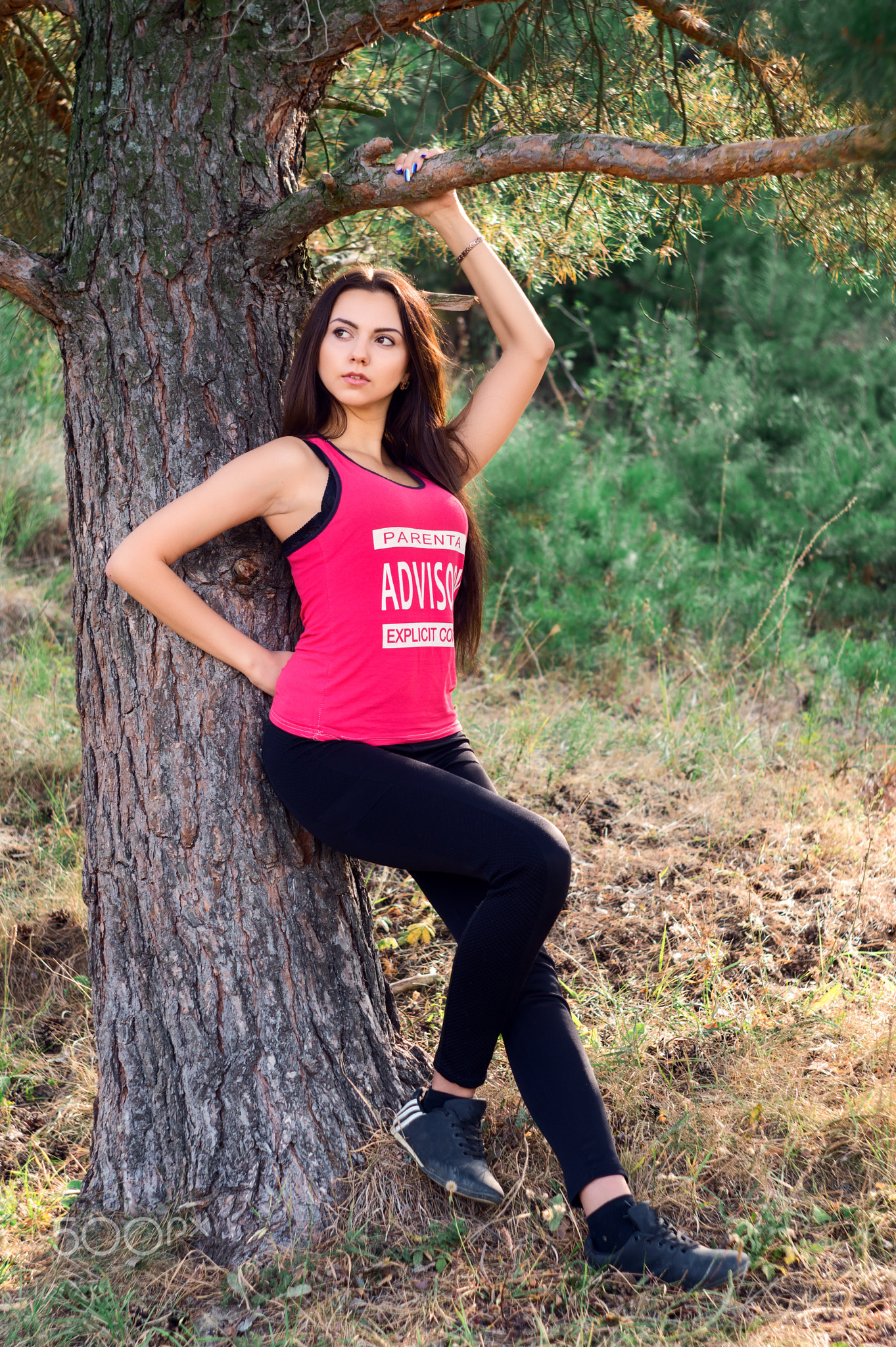 Young beautiful brunette model posing in the sports image of the park against the backdrop trees