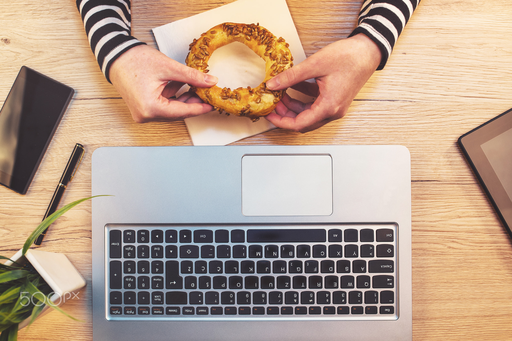 Woman eating sesame bagel for breakfast in office, top view