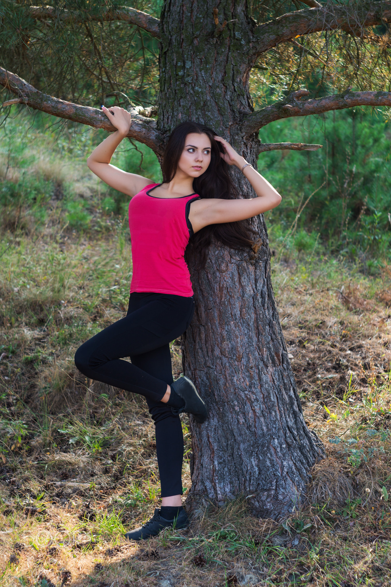 Young beautiful brunette model posing in the sports image of the park against the backdrop trees