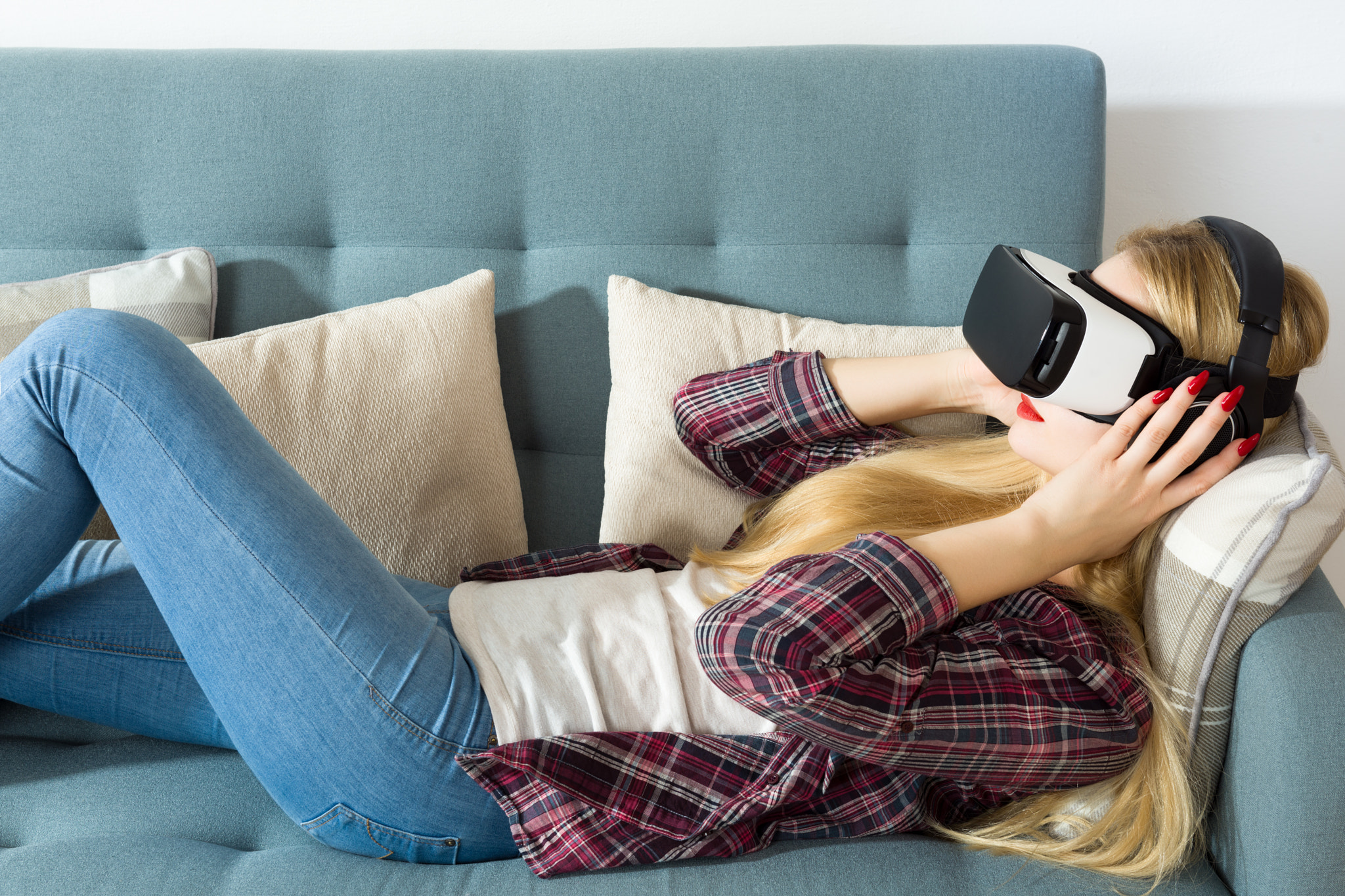 Attractive woman wearing virtual reality glasses lying on a couch. Virtual reality headset....