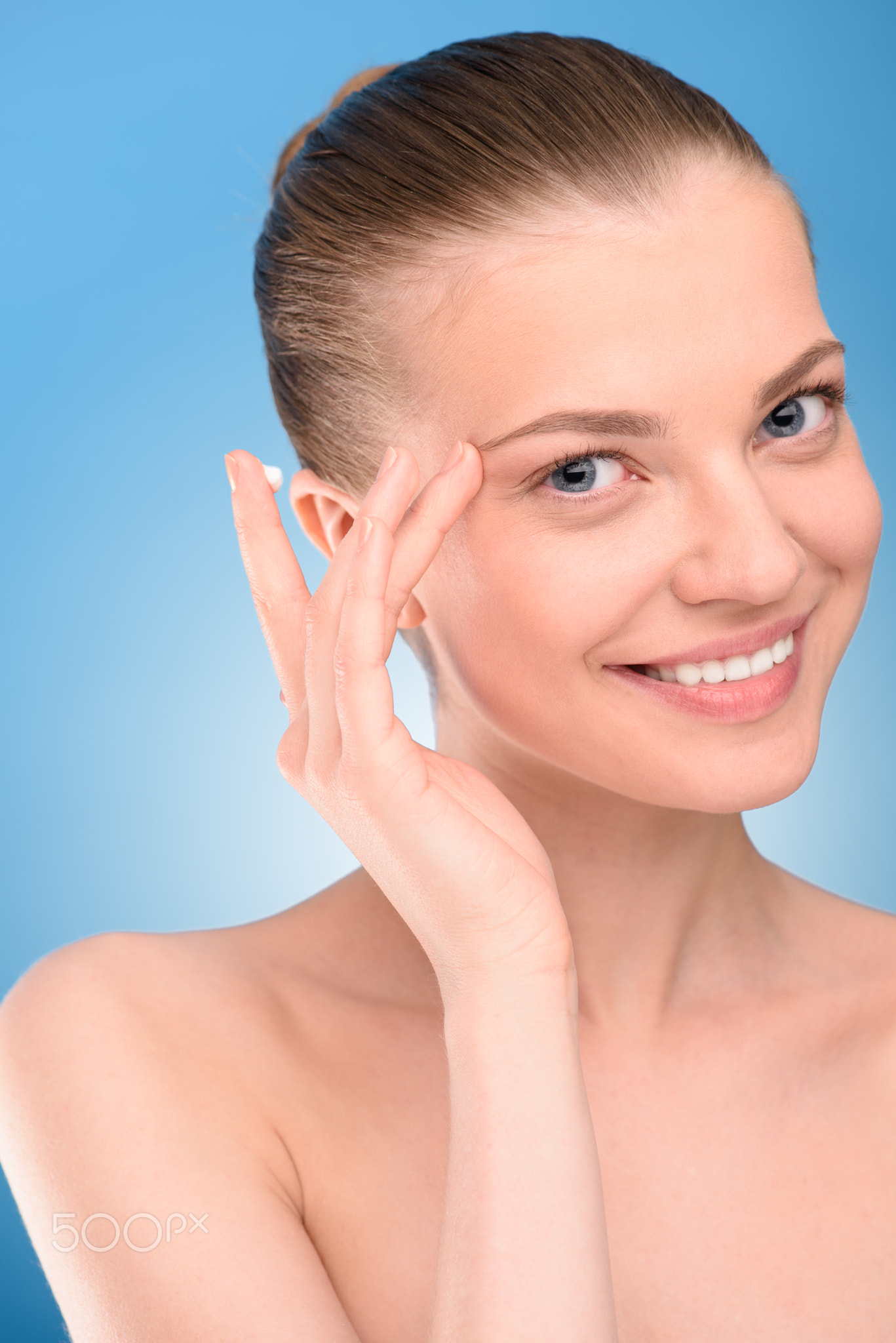 Woman applying lifting cream on face, over blue background.