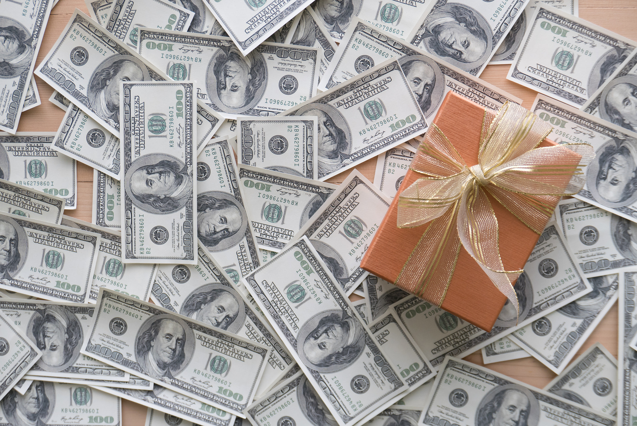 Yellow gift box with golden ribbons on pile of dollars banknotes