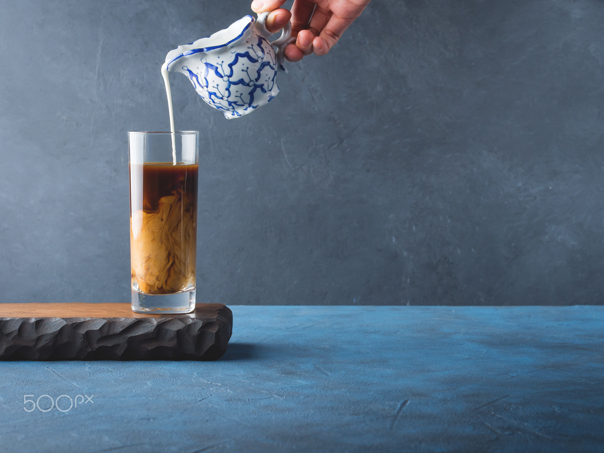 Pouring cream in glass of coffee on dark background