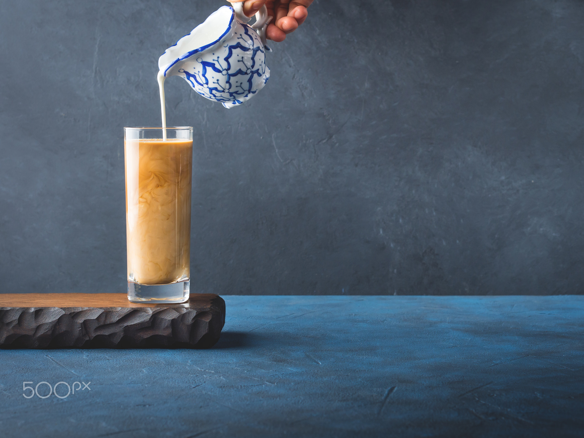 Pouring cream in glass of coffee on dark background