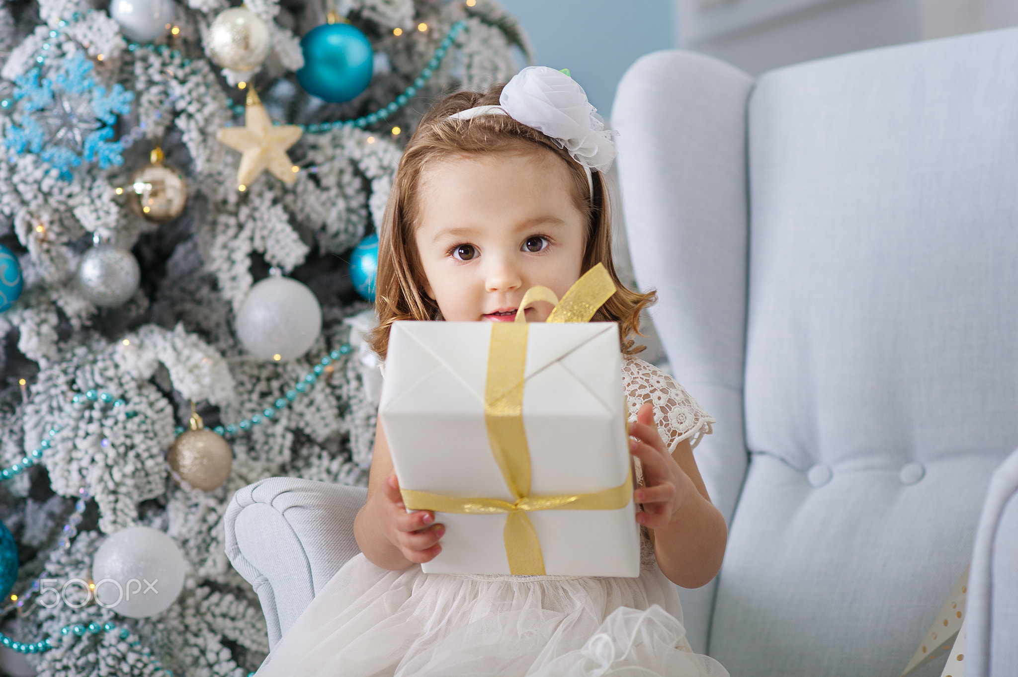 Portrait of cute little girl smiling and holding boxes with gifts near the Christmas tree. New...