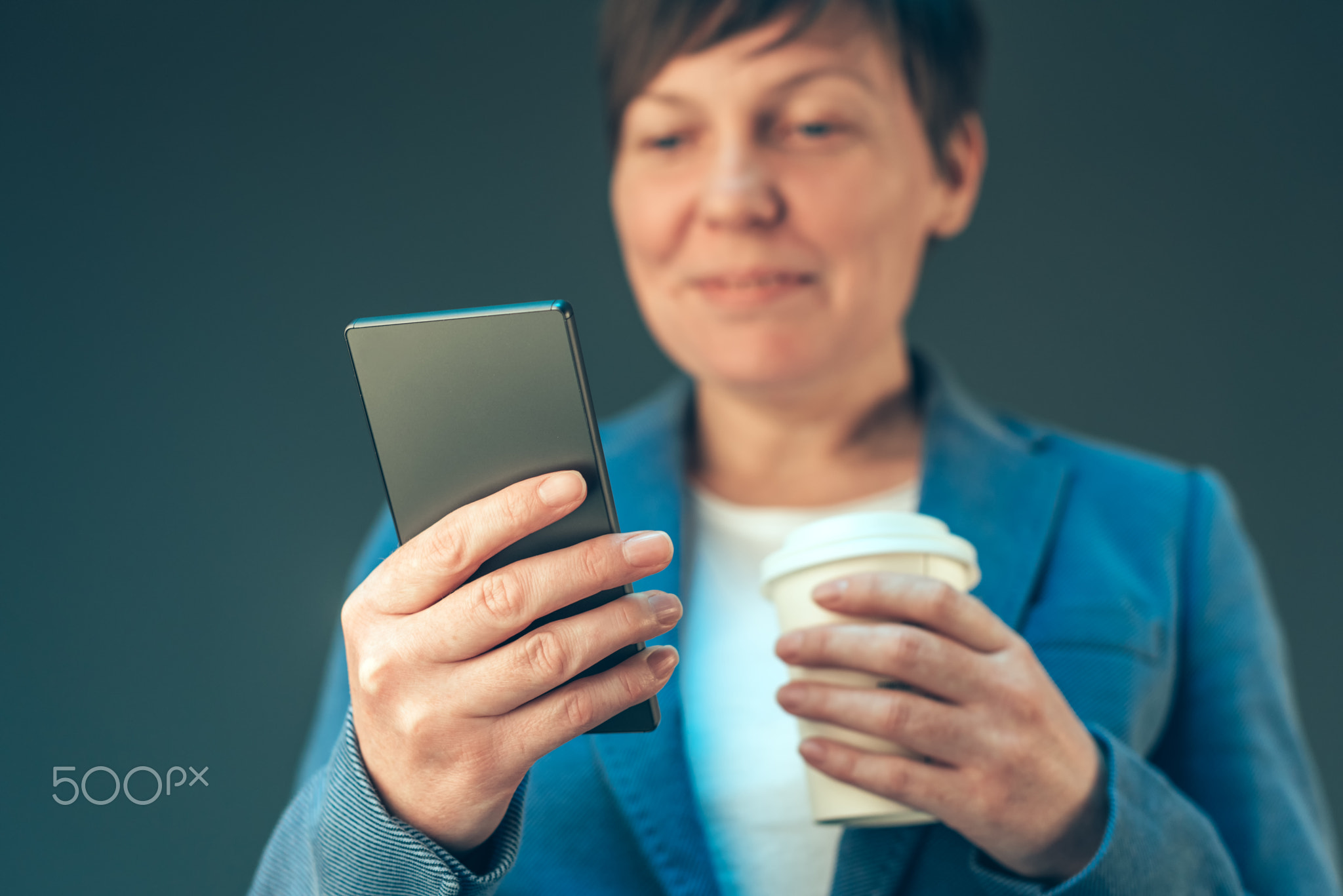 Satisfied businesswoman drinking coffee to go and looking mobile