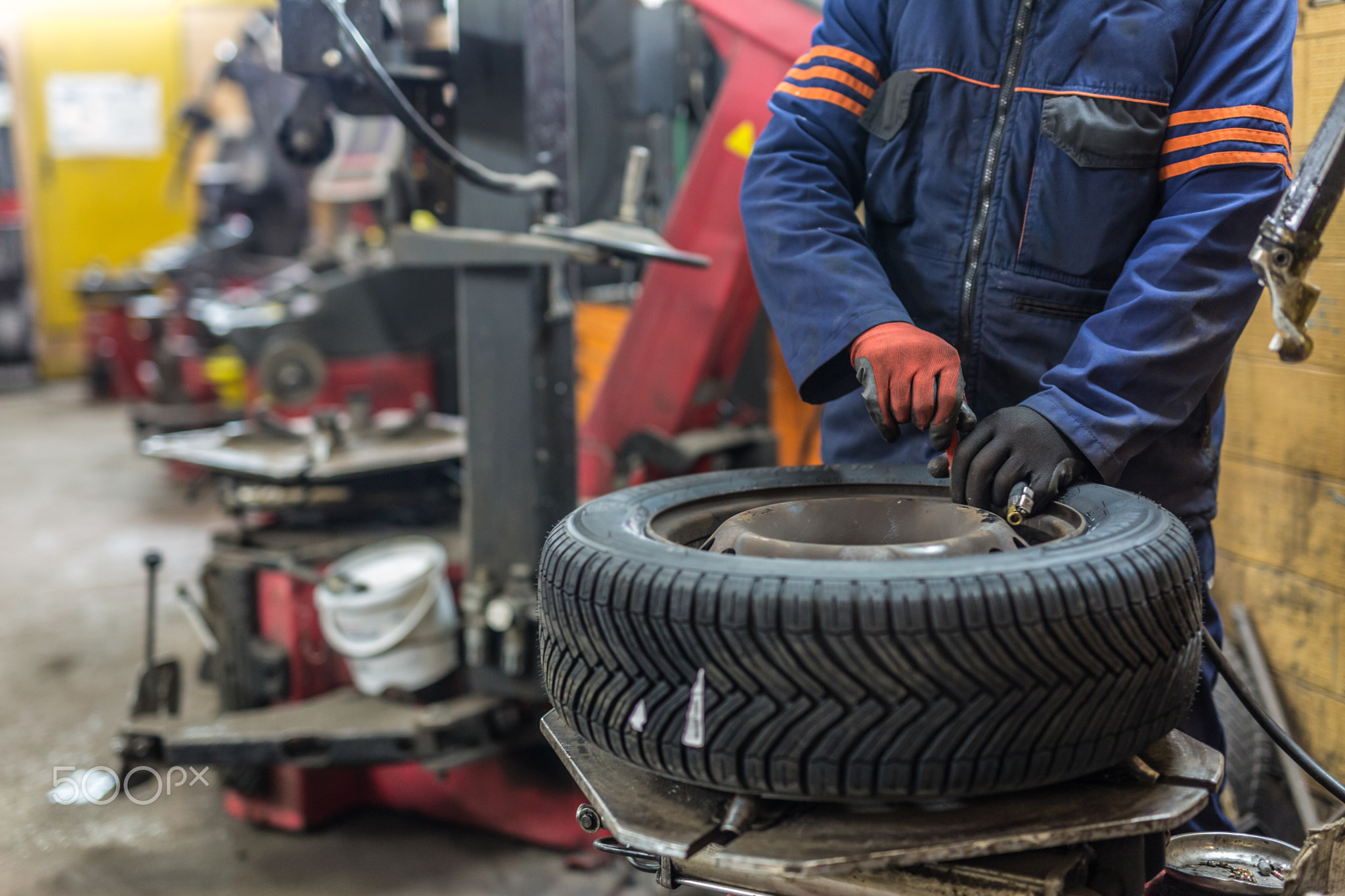 Professional auto mechanic replacing tire on wheel in car repair service.