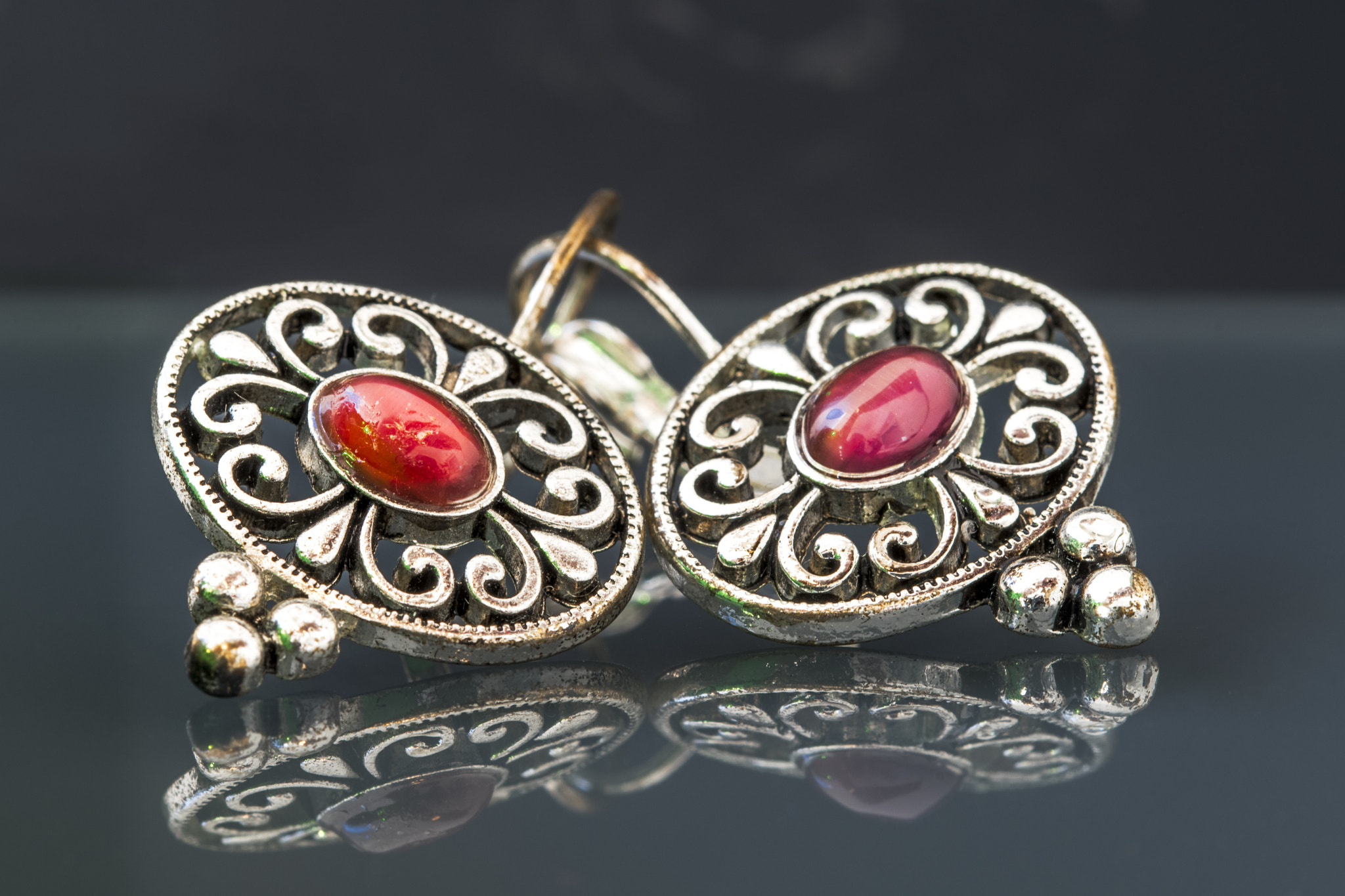 Nikon D500 sample photo. Silver earrings with red gems on dark background with reflection photography