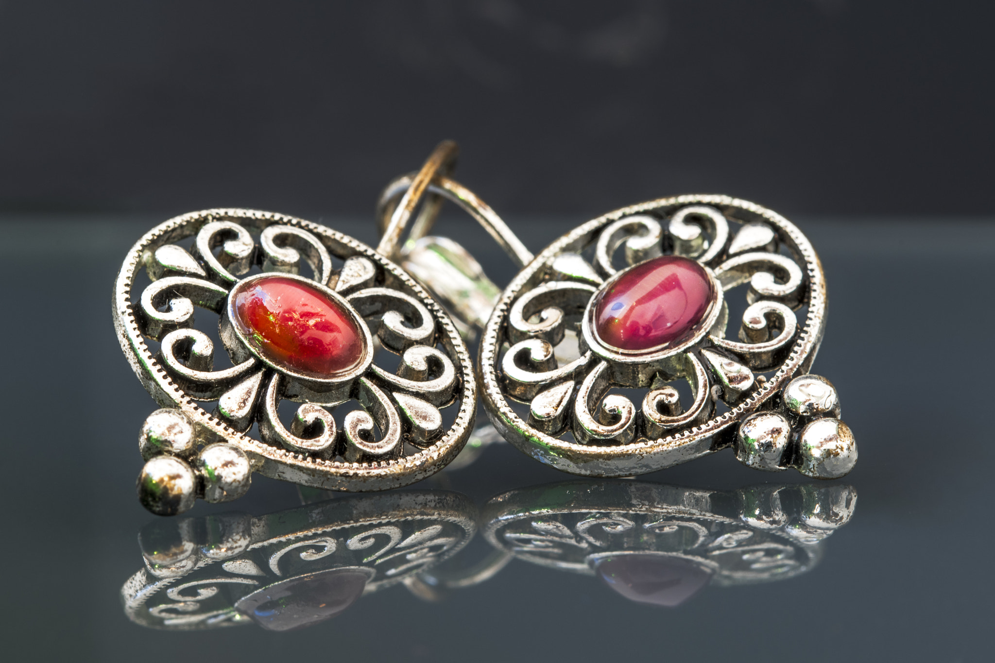 Sigma 105mm F2.8 EX DG OS HSM sample photo. Silver earrings with red gems on dark background with reflection photography