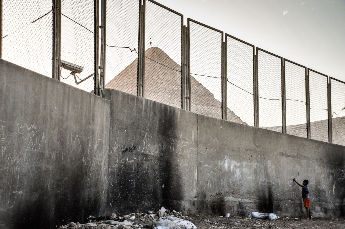 Nikon D700 + AF Zoom-Nikkor 24-120mm f/3.5-5.6D IF sample photo. A boy writes on the wall in front of cairo pyramids photography