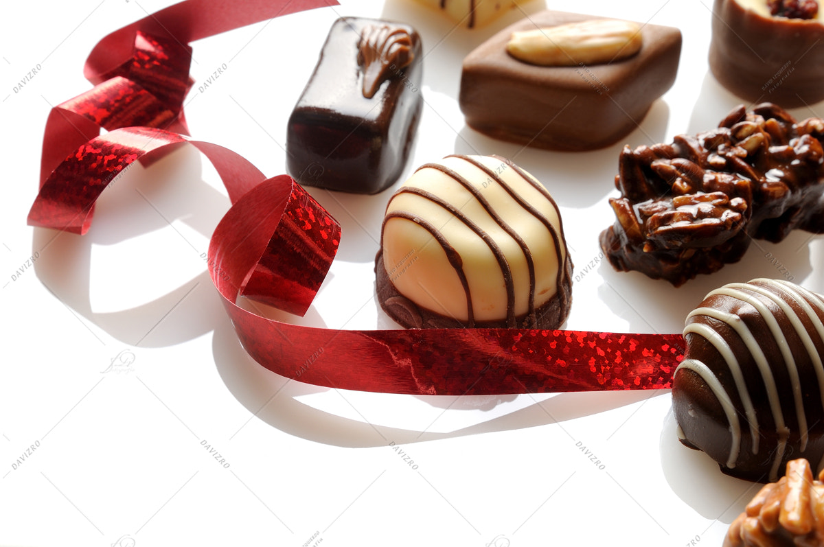 Nikon D300 sample photo. Assorted bonbons with red ribbon on a white table close-up photography