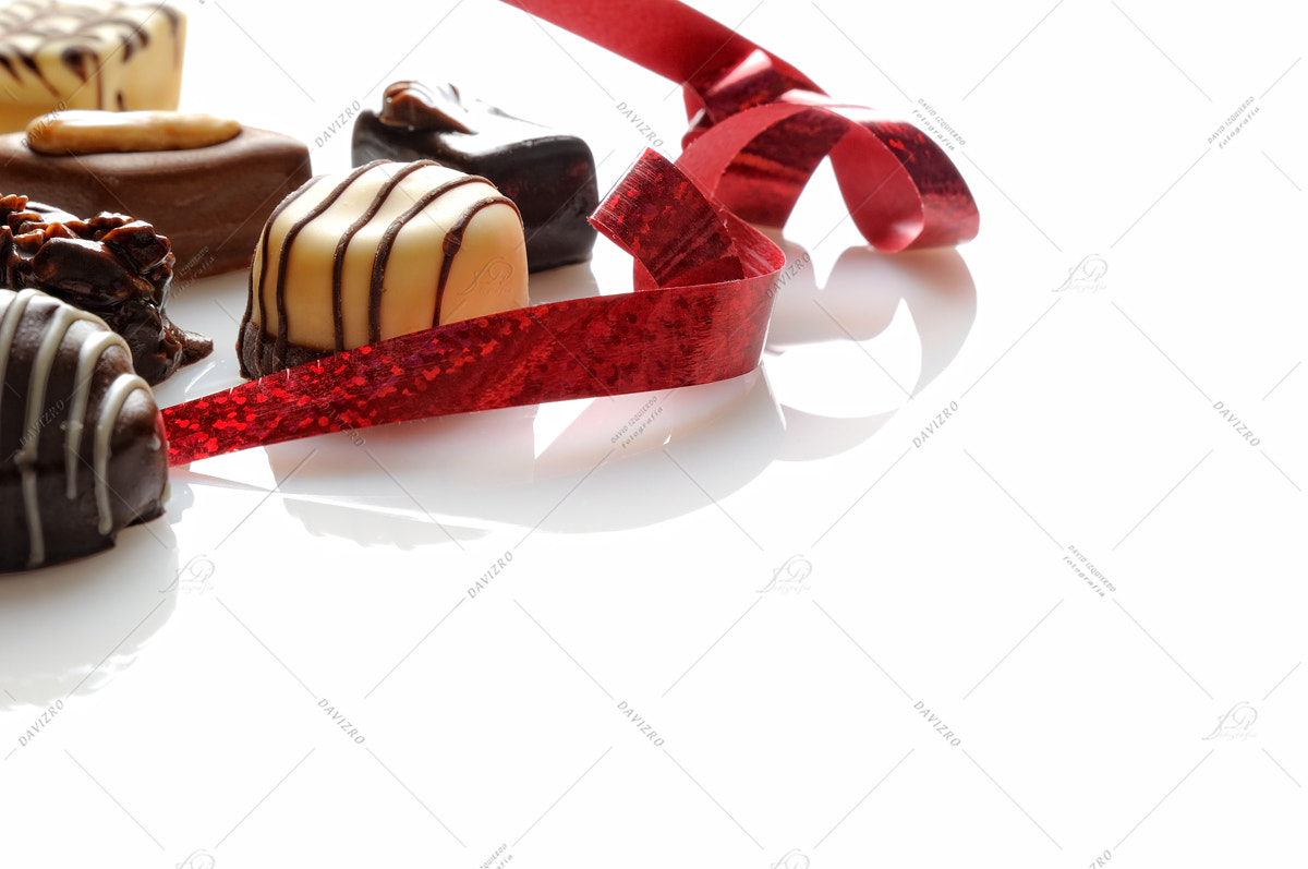 Nikon D300 sample photo. Assorted bonbons with red ribbon on a white table front photography