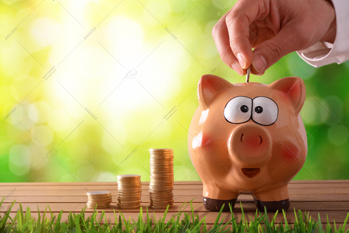 Hand putting money into piggy bank with green nature background