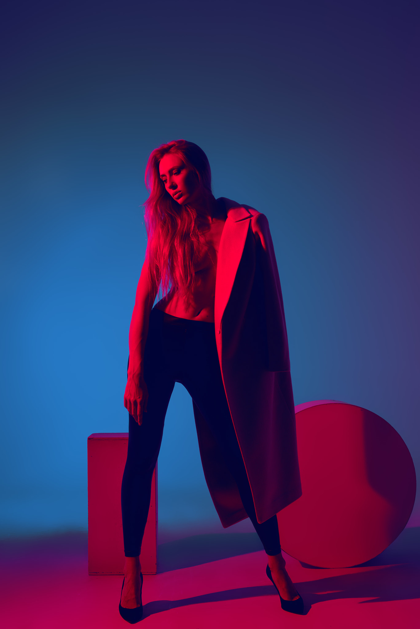 Fashion portrait of young girl in coat of black pants and heels in the studio with color filters....