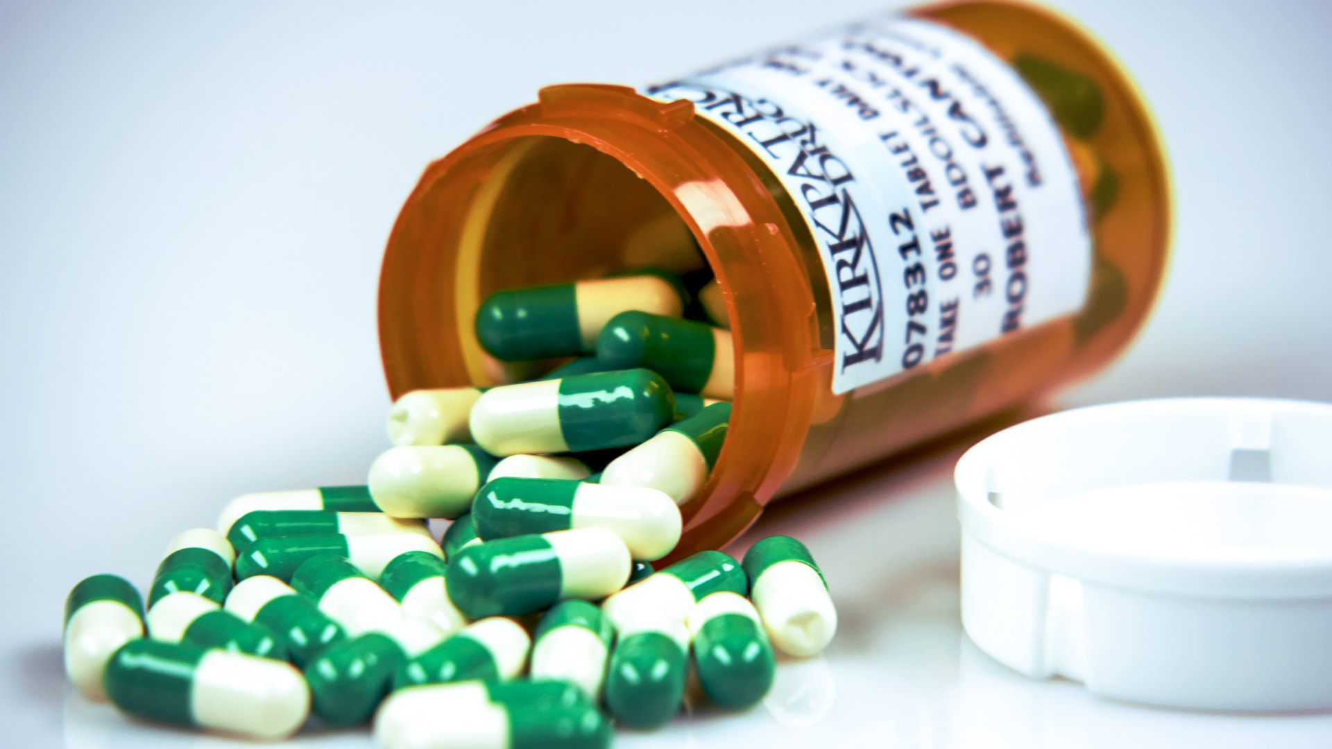Prescription bottle on its side containing green and white pills