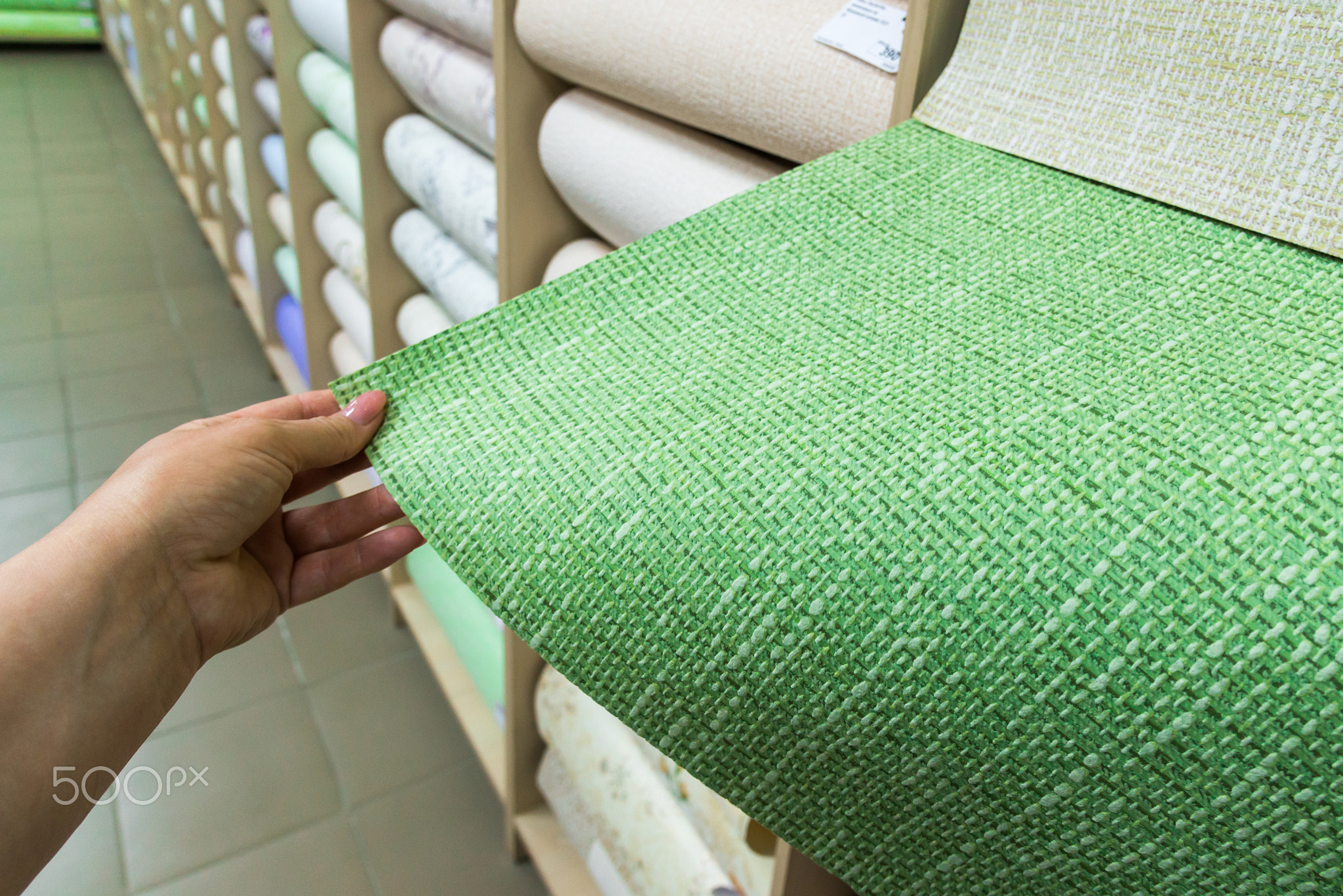 female hand holding green wallpaper in store