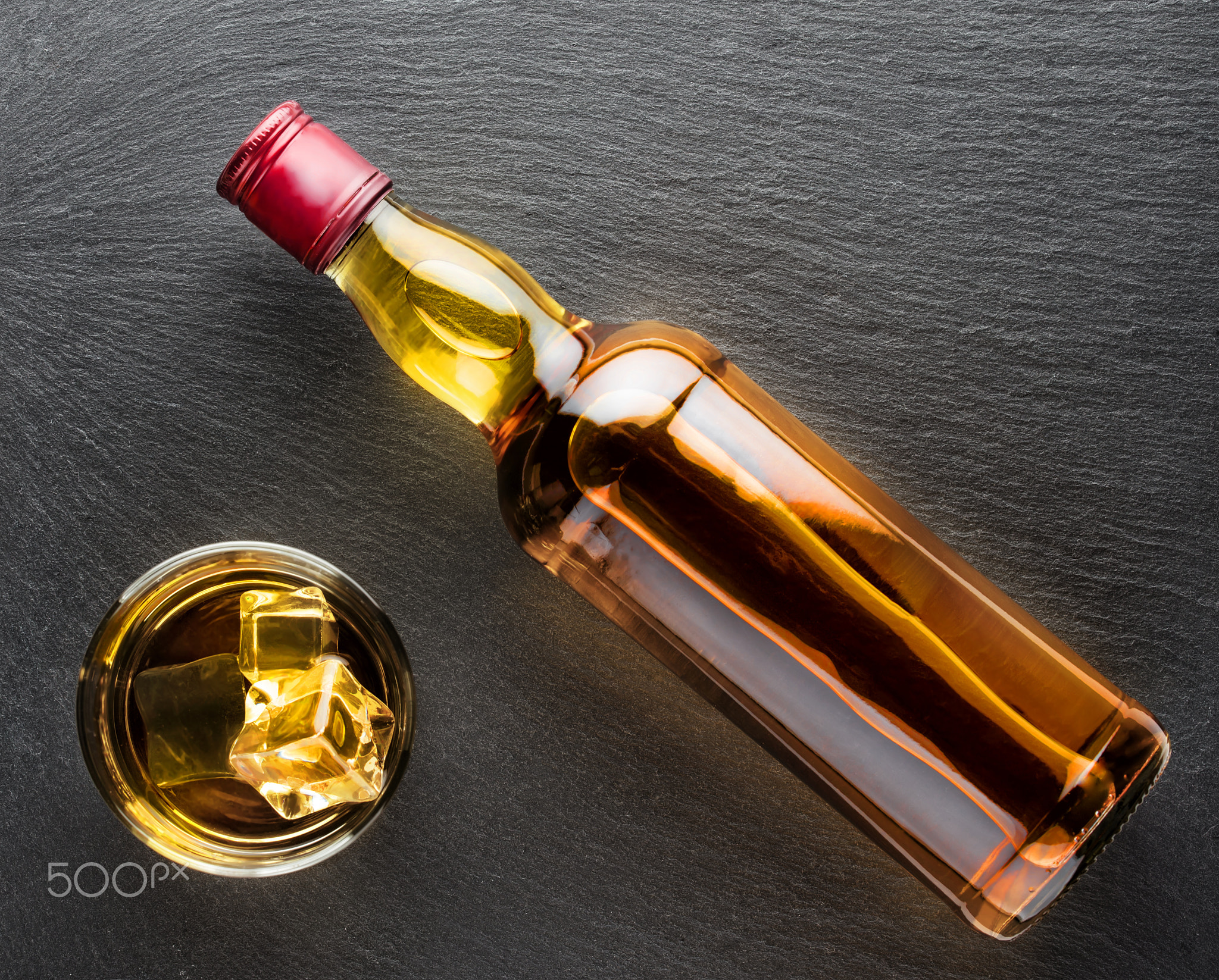 Glass of whiskey with ice and bottle