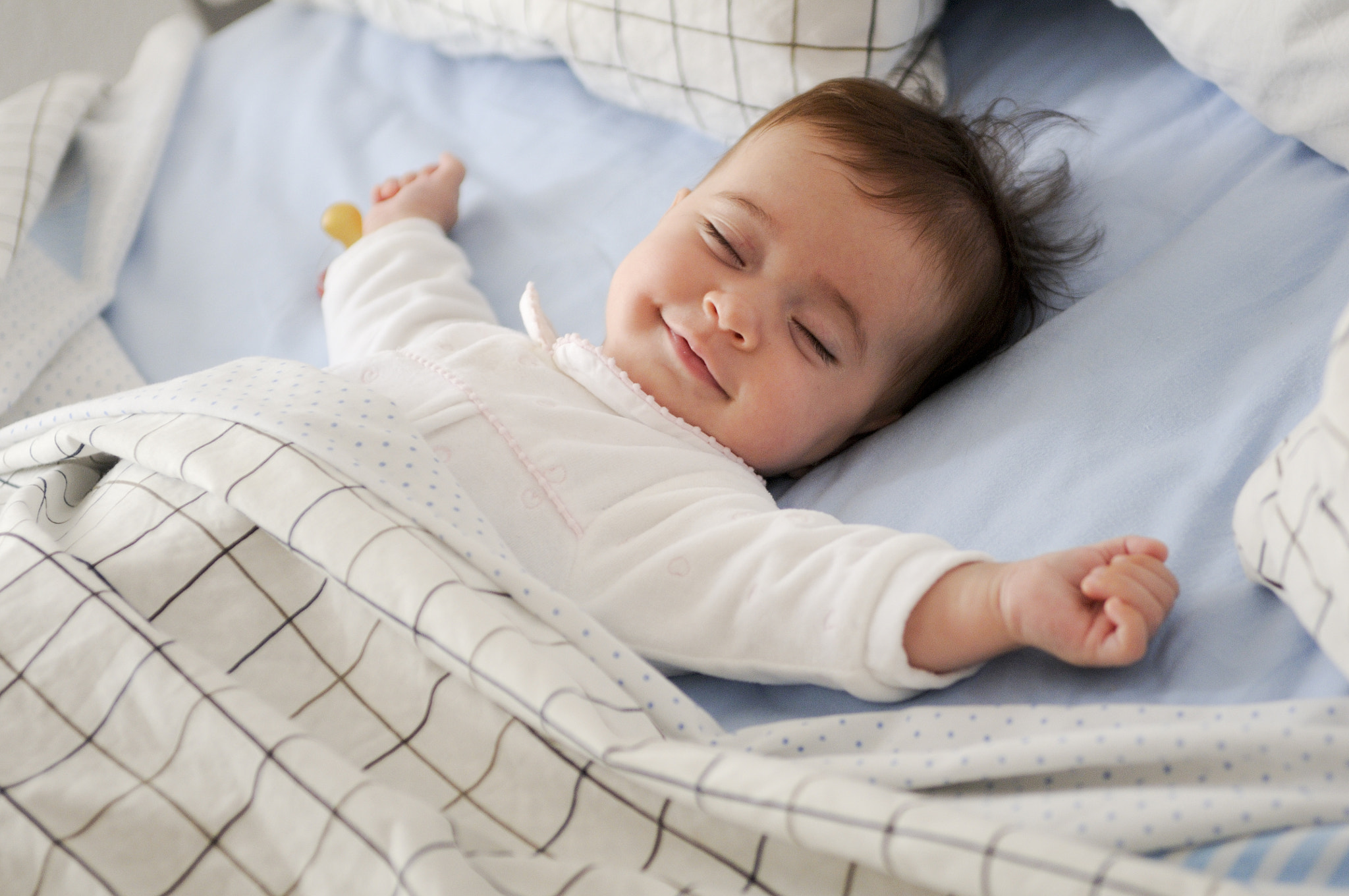 Nikon D300S sample photo. Smiling baby girl lying on a bed sleeping on blue sheets photography