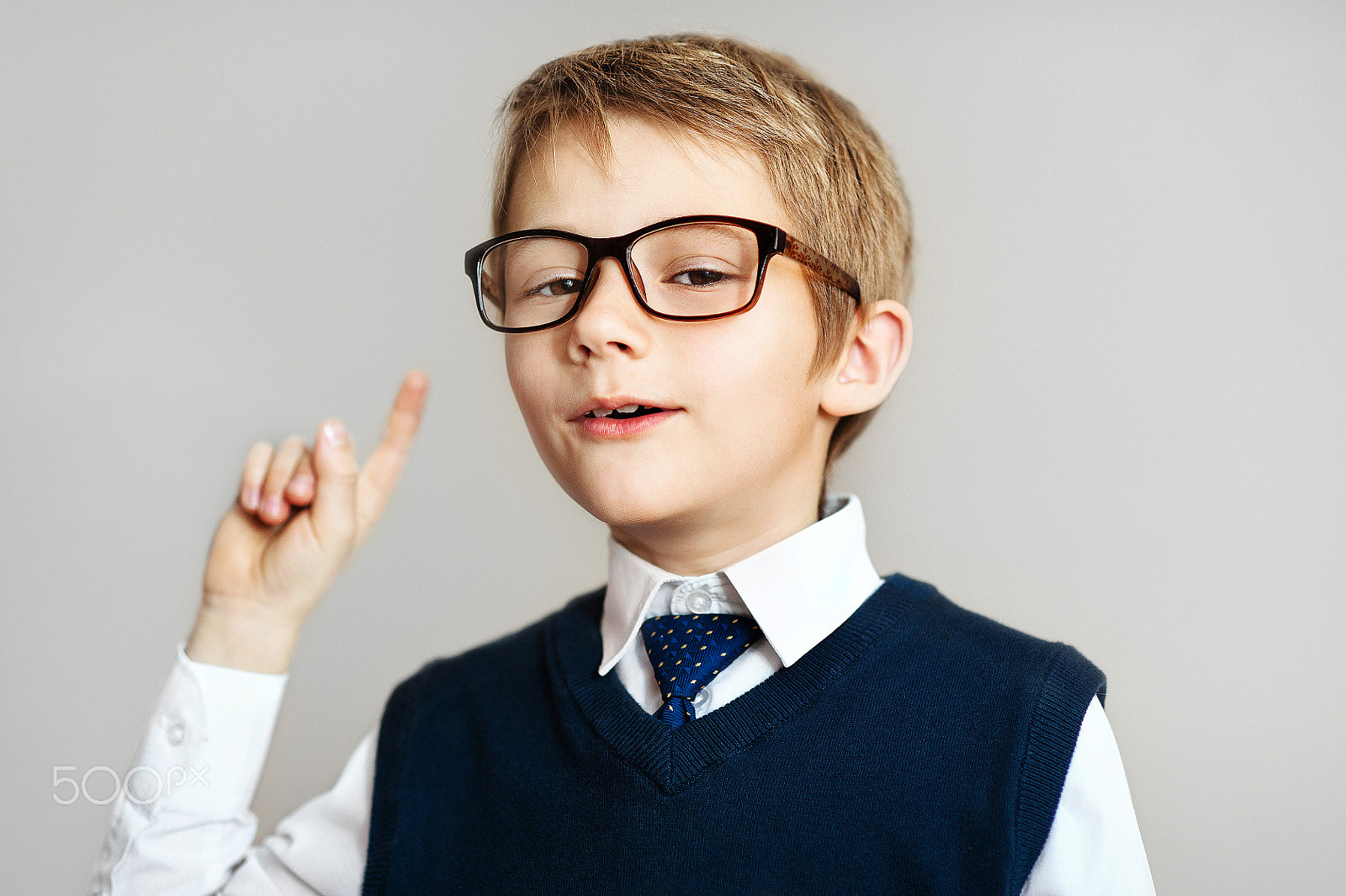 Nikon D700 + Nikon AF Nikkor 85mm F1.8D sample photo. Smiling young boy in big glasses showing finger up over gray background photography