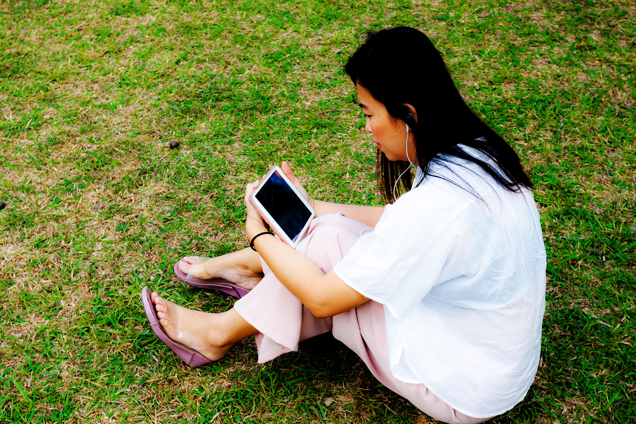 Young women using table ipad while sitting on grass in the park,