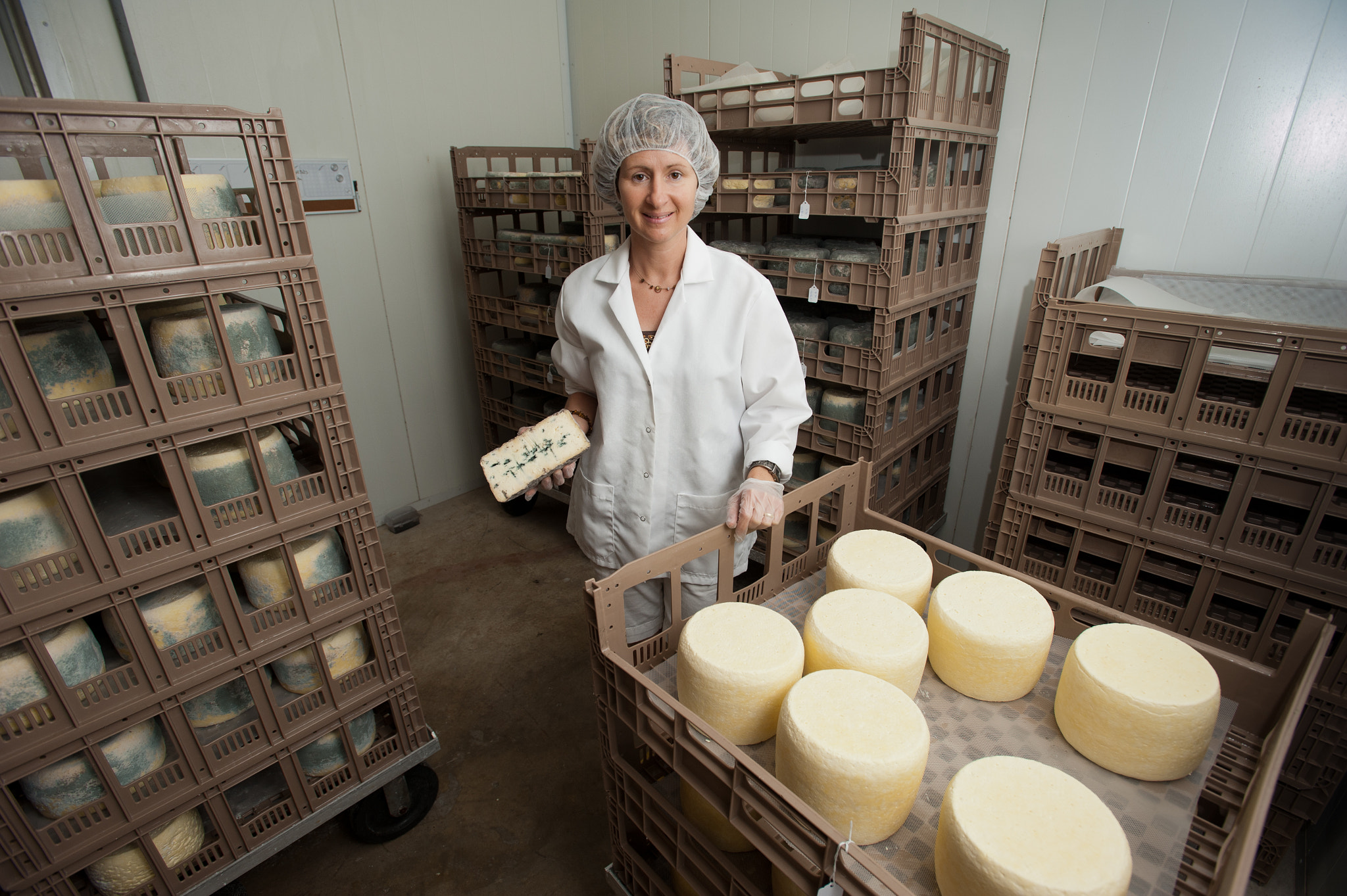 Nikon D700 + Nikon AF-S Nikkor 17-35mm F2.8D ED-IF sample photo. Woman posing with wheels of homemade cheeses at creamery photography