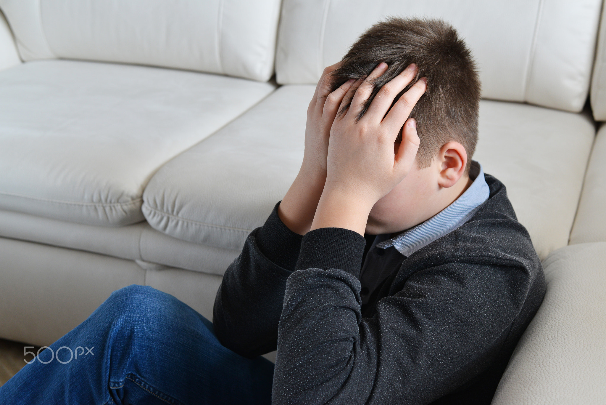 Upset teenager 13 years, he sits near sofa covering her face with her hands