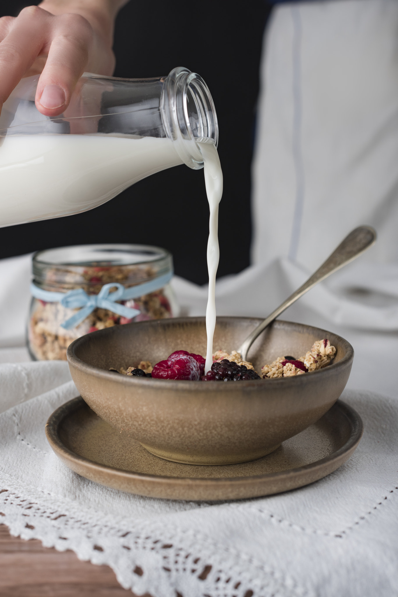 Human pours milk into a bowl with muesli.